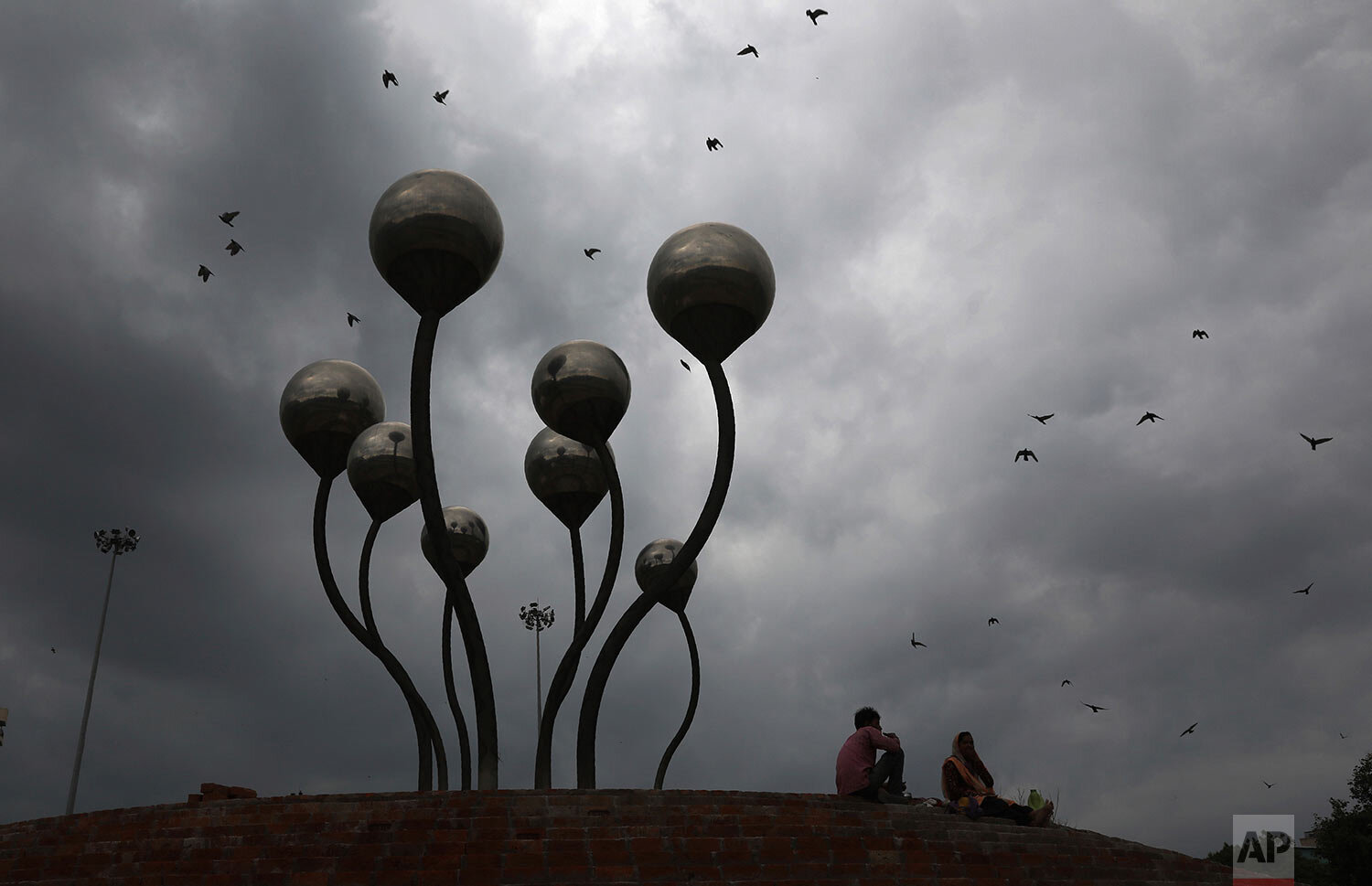  A couple rest next to a sculpture as the sky fills up with heavy monsoon rain clouds in New Delhi, India, Sunday, Aug. 30, 2020. (AP Photo/Manish Swarup) 
