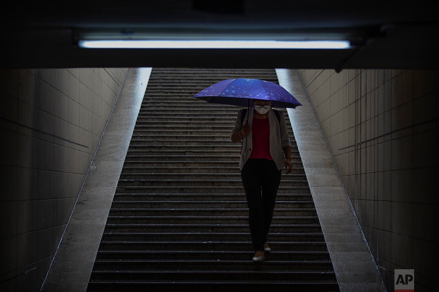  A woman wearing a face mask to protect against the coronavirus walks into the entrance of a subway station during rainfall in Beijing, Wednesday, Aug. 5, 2020.  (AP Photo/Mark Schiefelbein) 