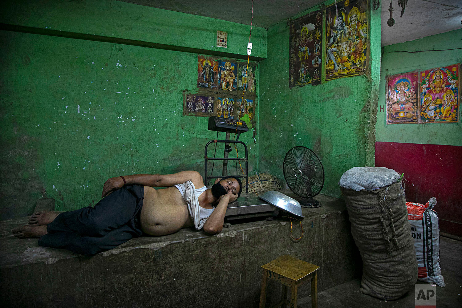  An Indian man sleeps as photographs of Hindu Gods are seen pasted on the walls of his shop, in a wholesale vegetable market in Gauhati, India, Thursday, Aug. 27, 2020.  (AP Photo/Anupam Nath) 