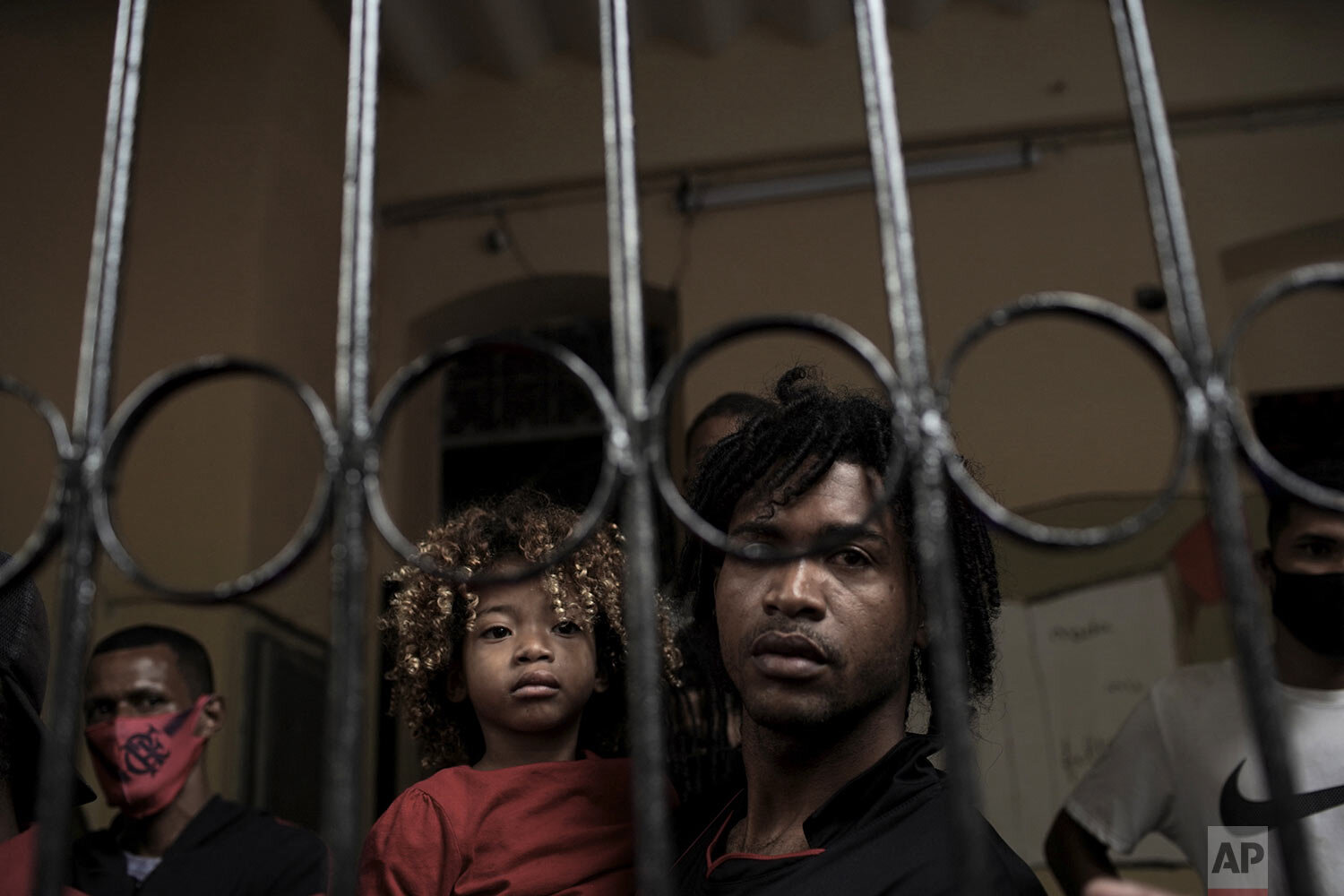  A man holds a child behind the gate of a house occupied by squatters for close to a year, before they are evicted in Rio de Janeiro, Brazil, Sept.15, 2020, amid the new coronavirus pandemic. (AP Photo/Silvia Izquierdo) 