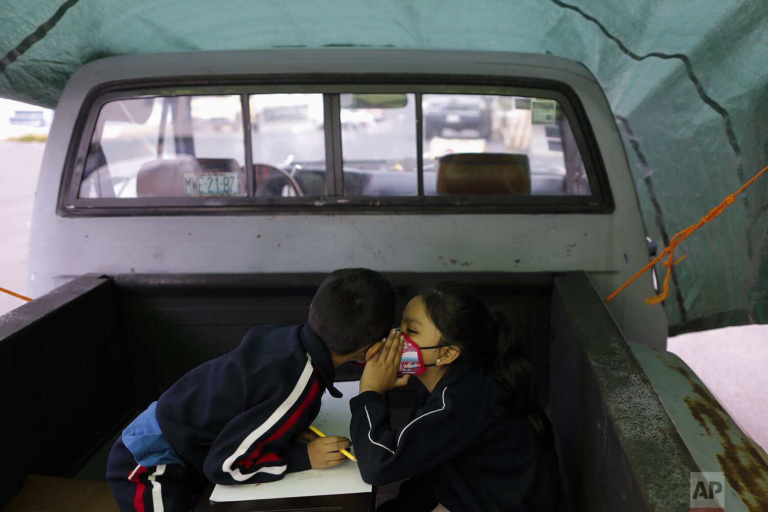  Paulina Mariano Ortiz whispers to her brother Axel in the bed of a pick-up truck that was repurposed as an educational space on the southern edge of Mexico City, Sept. 4, 2020. Concerned about the educational difficulties facing school-age children 