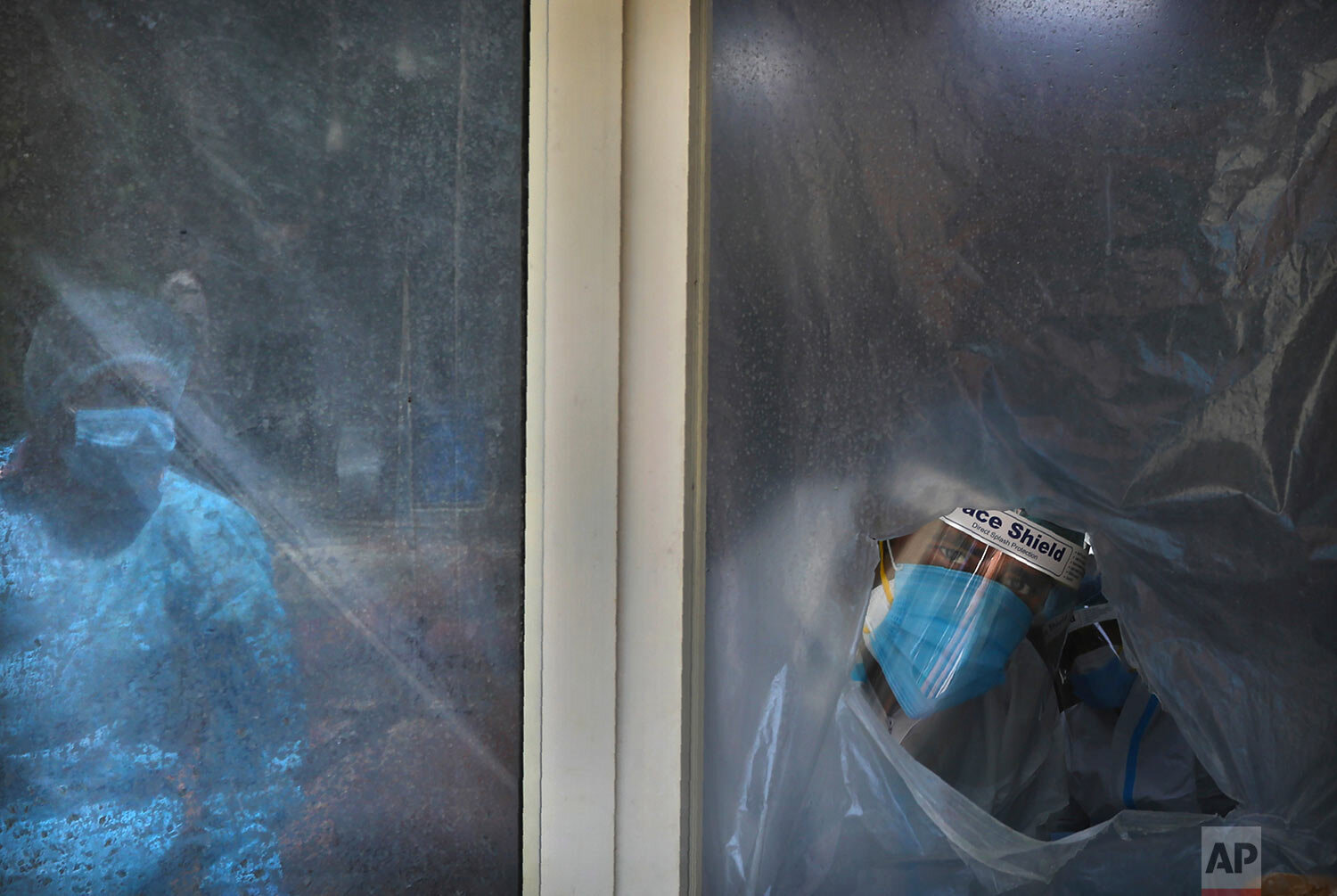  A health worker looks out from behind the plastic sheet covered window from where he conducts tests for COVID-19 in New Delhi, India, Saturday, Sept. 5, 2020.  (AP Photo/Manish Swarup) 