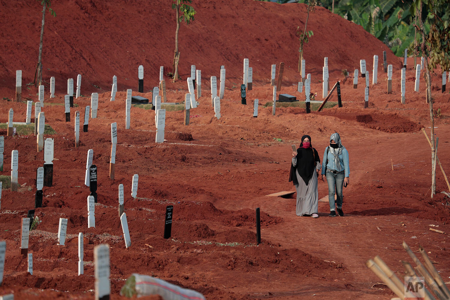  Indonesian Muslim women walk near grave marks at the special section of Pondok Ranggon cemetery which was opened to accommodate the surge in deaths during coronavirus outbreak in Jakarta, Indonesia, Thursday, Sept. 24, 2020. (AP Photo/Dita Alangkara