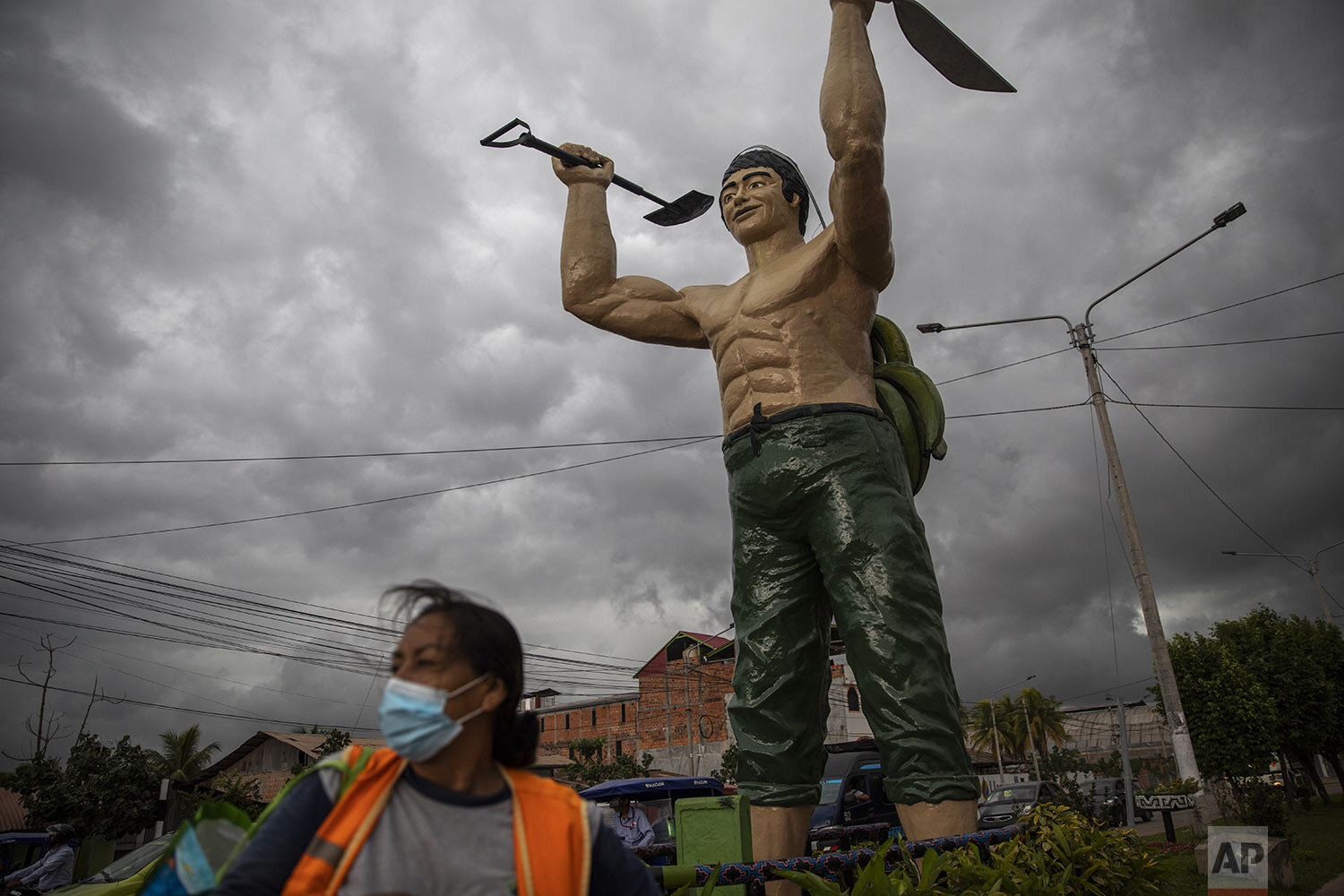  A woman using a protective face mask amid the new cornavirus pandemic, stands next to the monument "El hombre Chacarero,” that represents a rural worker, in Pucallpa, Ucayali region, Peru, Monday, Sept. 28, 2020. (AP Photo/Rodrigo Abd) 