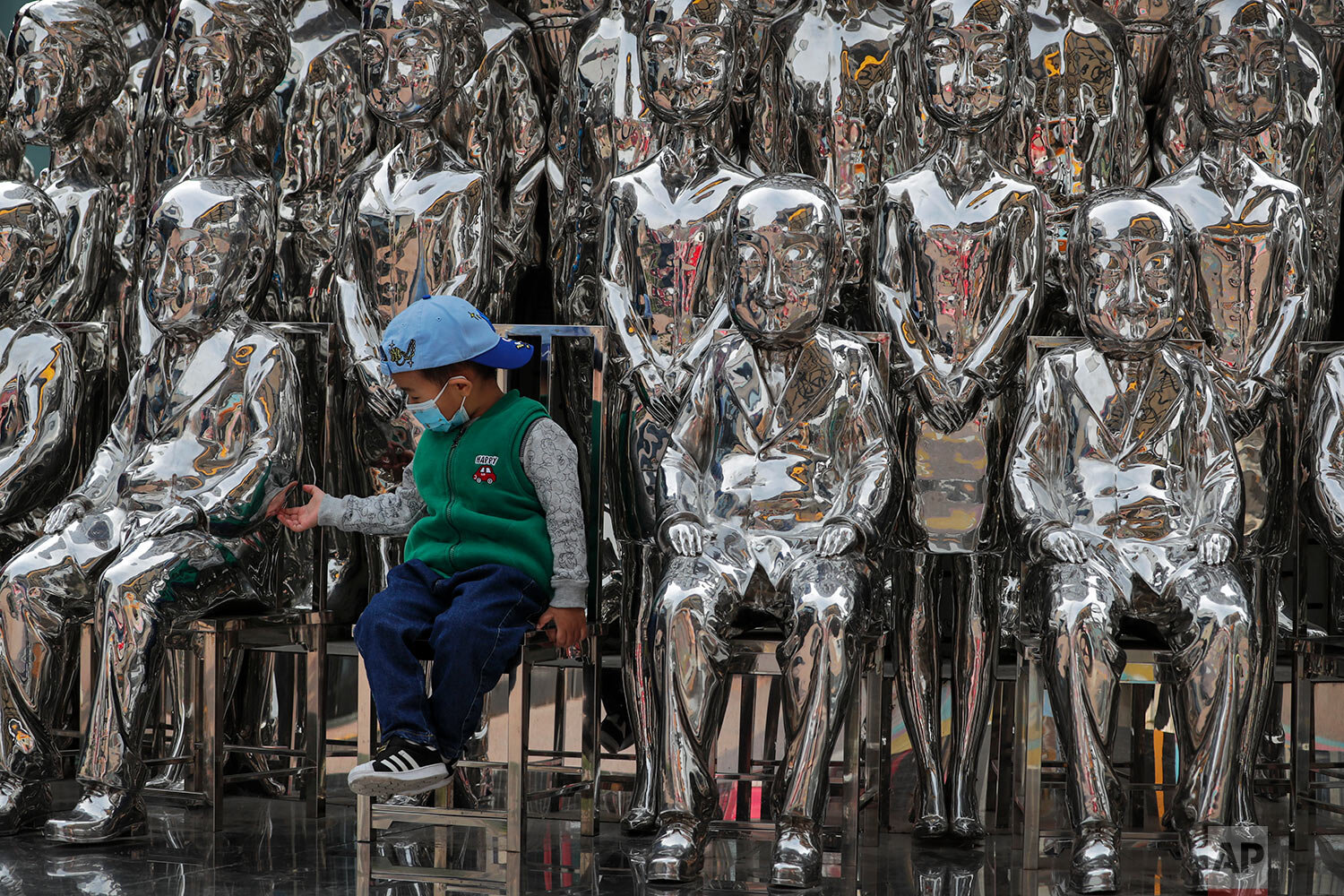  A child wearing a face mask to help curb the spread of the coronavirus tries to hold a statue's hand as he sits in an art installation on display at a shopping mall in Beijing, Sunday, Oct. 11, 2020. (AP Photo/Andy Wong) 