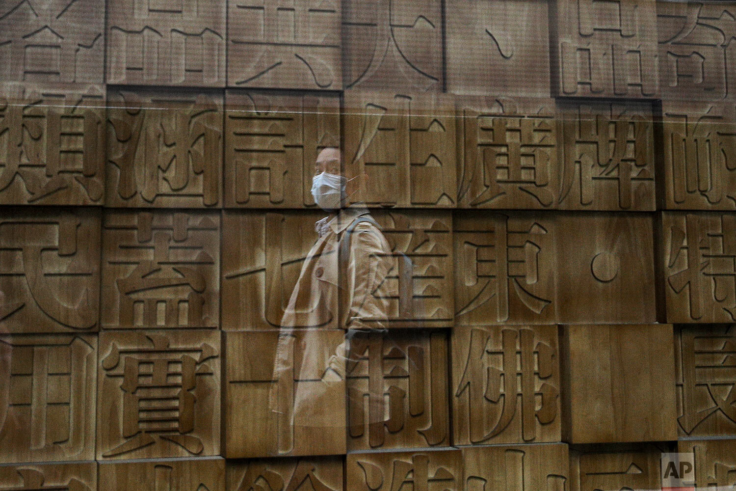  A woman wearing a face mask to help curb the spread of the coronavirus is reflected on a window panel as she walks by a retailed shop displaying Chinese calligraphy fonts in Beijing, Wednesday, Oct. 14, 2020. (AP Photo/Andy Wong) 