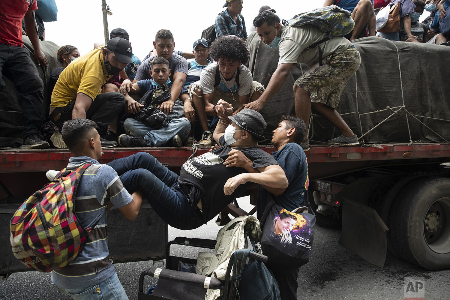  Wheelchair bound migrant Wilmer Chavez, 33, is helped by fellow migrants on to the back of a freight truck that stopped to give the migrants a free ride in Rio Dulce, Guatemala, Oct. 2, 2020. (AP Photo/Moises Castillo) 