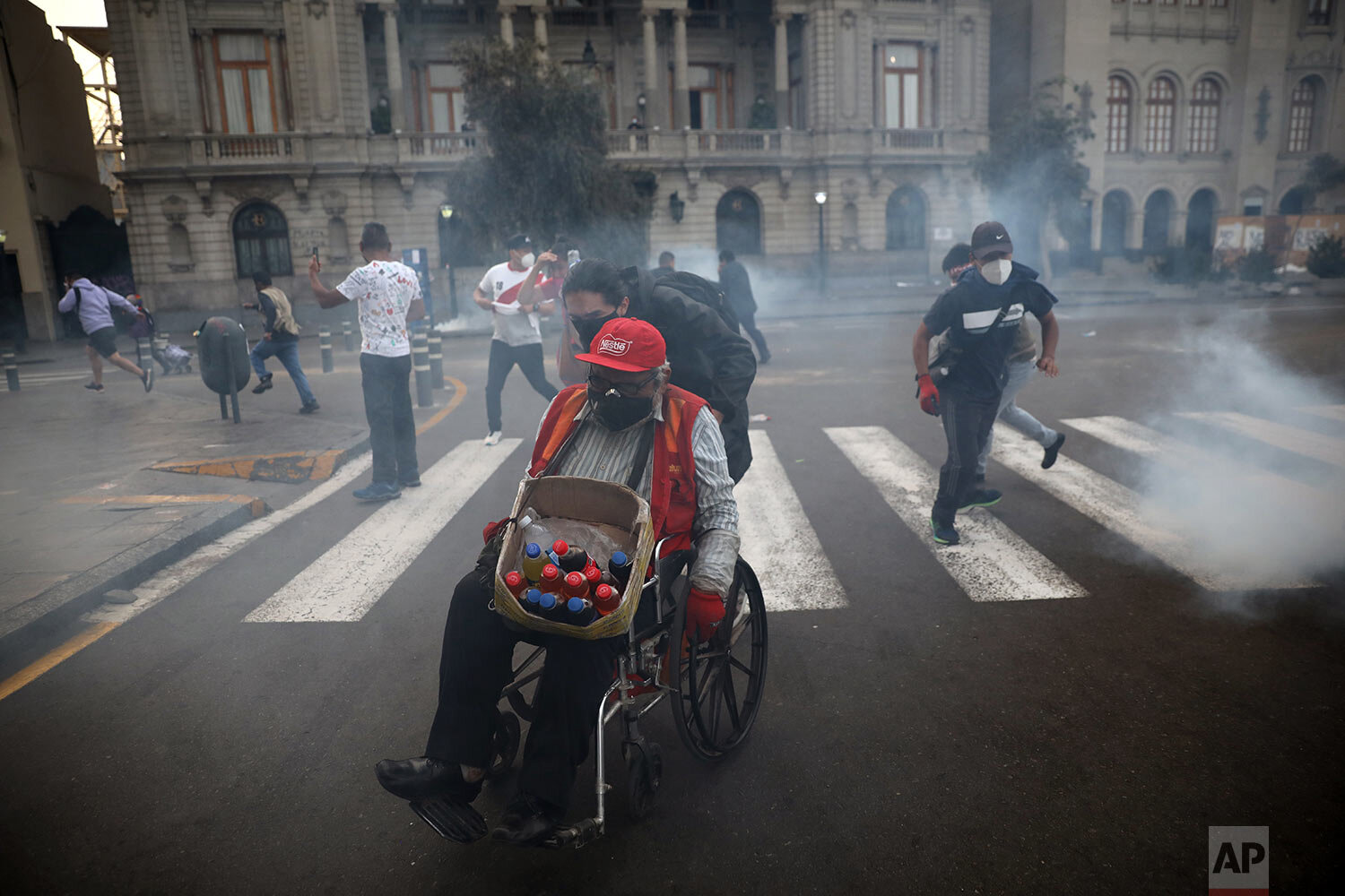  A protester helps a vendor in a wheelchair seek refuge from tear gas launched by police to disperse protesters near Congress where lawmakers swore-in a new president after voting to oust President Martin Vizcarra the day before, in Lima, Peru, Tuesd