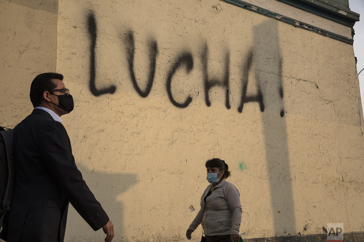  Pedestrians walk past a wall spray-painted by an anti-government protester with the Spanish word for fight, just a block from the Justice Palace where people who are refusing to recognize Peru's new government gathered to protest, in Lima, Wednesday