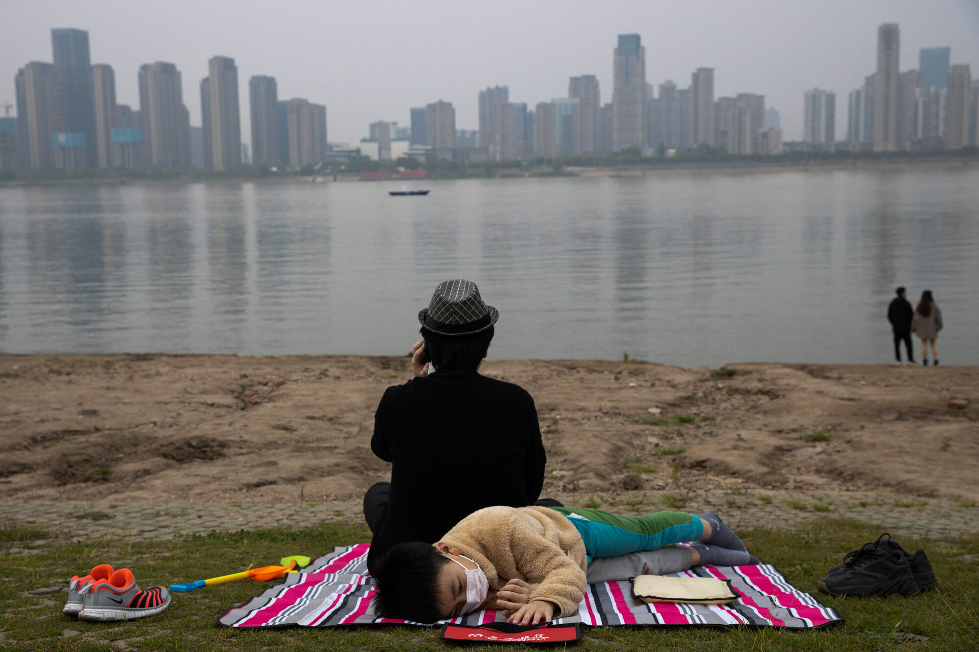 A child wearing a mask to protect against the coronavirus rests on the bank of the Yangtze River in Wuhan in central China's Hubei province on April 16, 2020. (AP Photo/Ng Han Guan)
