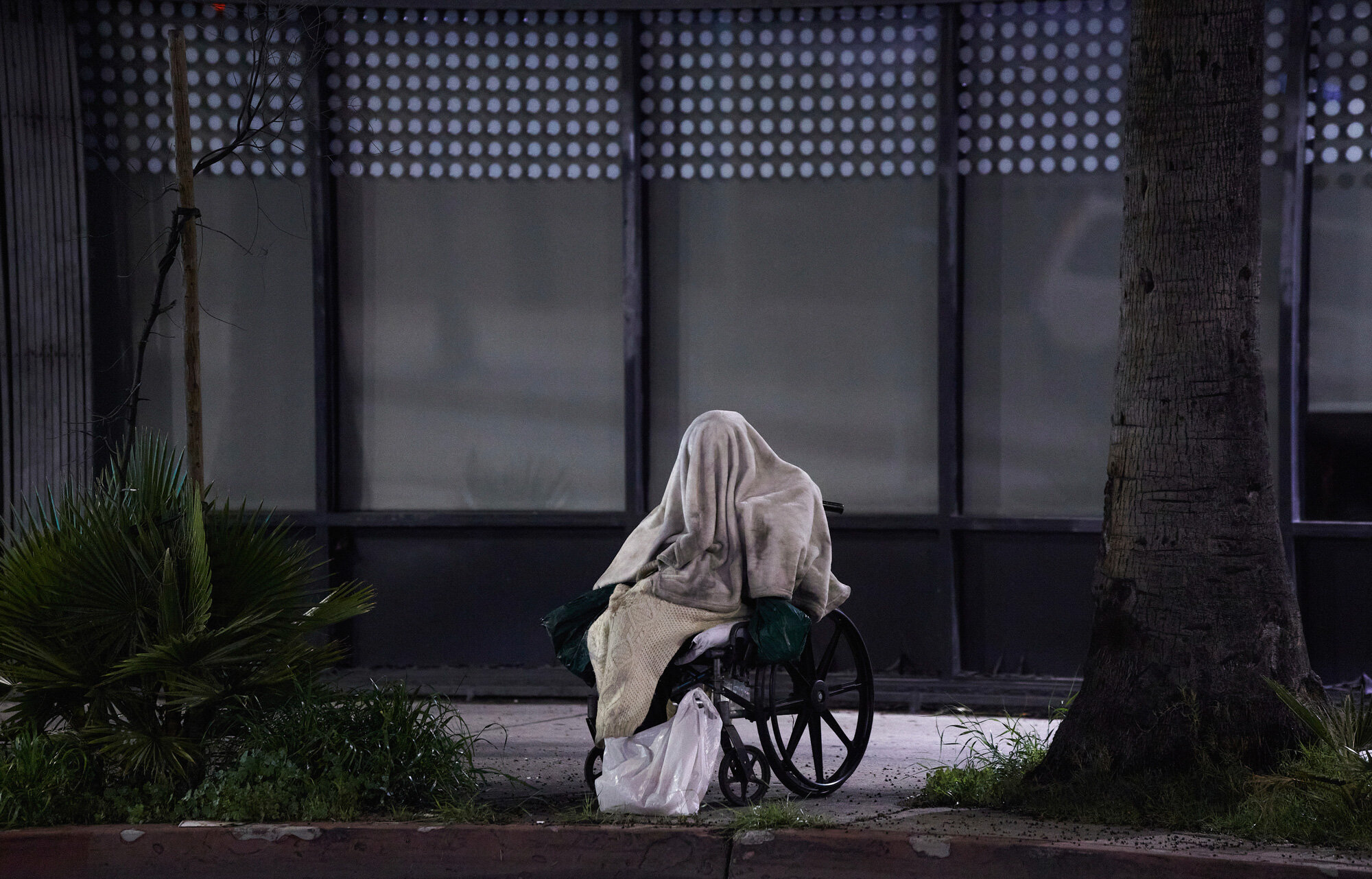 A homeless person sits in a wheelchair during rainy weather on Sunset Blvd. in the Echo Park neighborhood of Los Angeles on April 6, 2020. California Gov. Gavin Newsom signed an emergency order in mid-March to spend $150 million to help the homeless during the pandemic. (AP Photo/Damian Dovarganes)