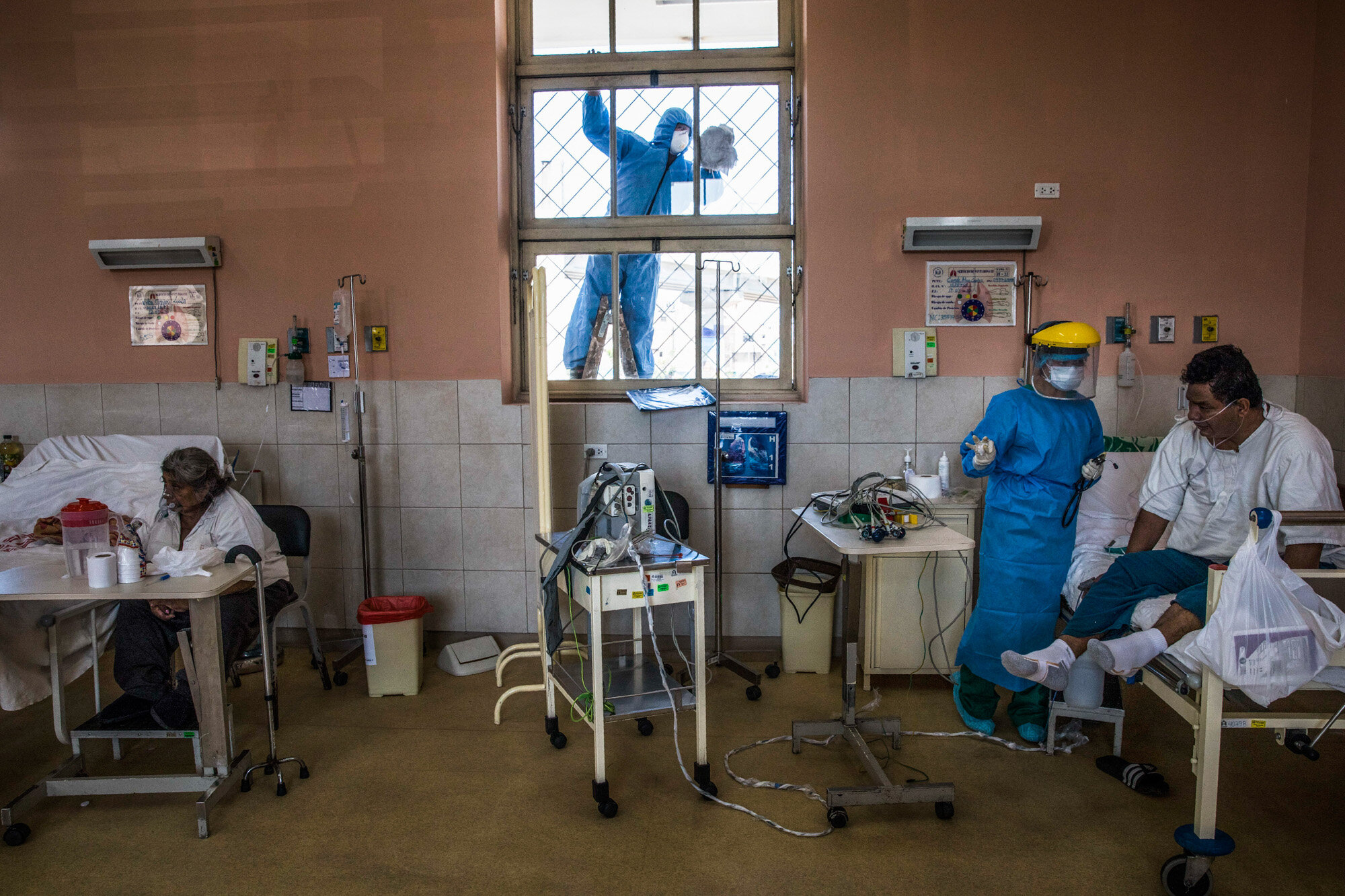 A worker wearing protective gear cleans a window as a nurse tends to a patient inside the intensive care unit for people infected with the coronavirus at the 2 de Mayo Hospital in Lima, Peru, on April 17, 2020. (AP Photo/Rodrigo Abd)