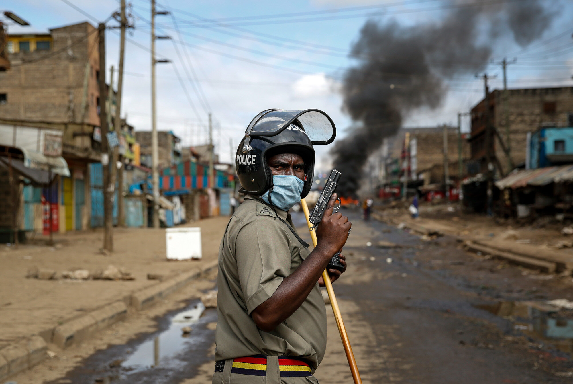 A police officer holds a pistol during clashes with protesters near a barricade of burning tires in the Kariobangi slum of Nairobi, Kenya, on May 8, 2020. Hundreds of protesters blocked one of the capital's major highways to protest government demolitions of the homes of more than 7,000 people, causing many to sleep out in the rain and cold because of restrictions on movement due to the coronavirus. (AP Photo/Brian Inganga)