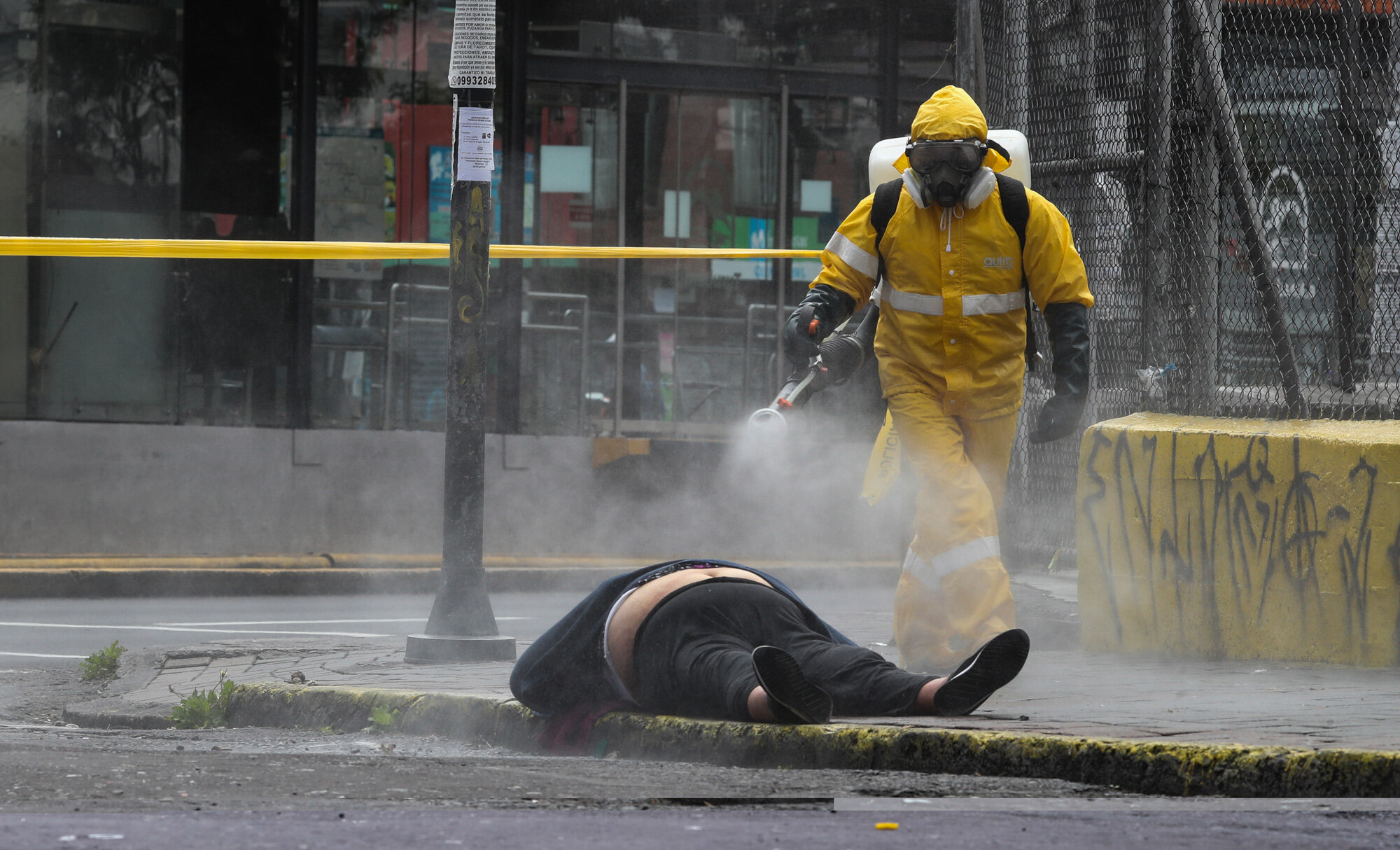 A worker from the city's forensic department in Quito, Ecuador, sprays disinfectant over the body of a woman who died on the street on May 14, 2020. Forensic workers at the scene conducted a COVID-19 rapid test and said the woman tested negative. (AP Photo/Dolores Ochoa)
