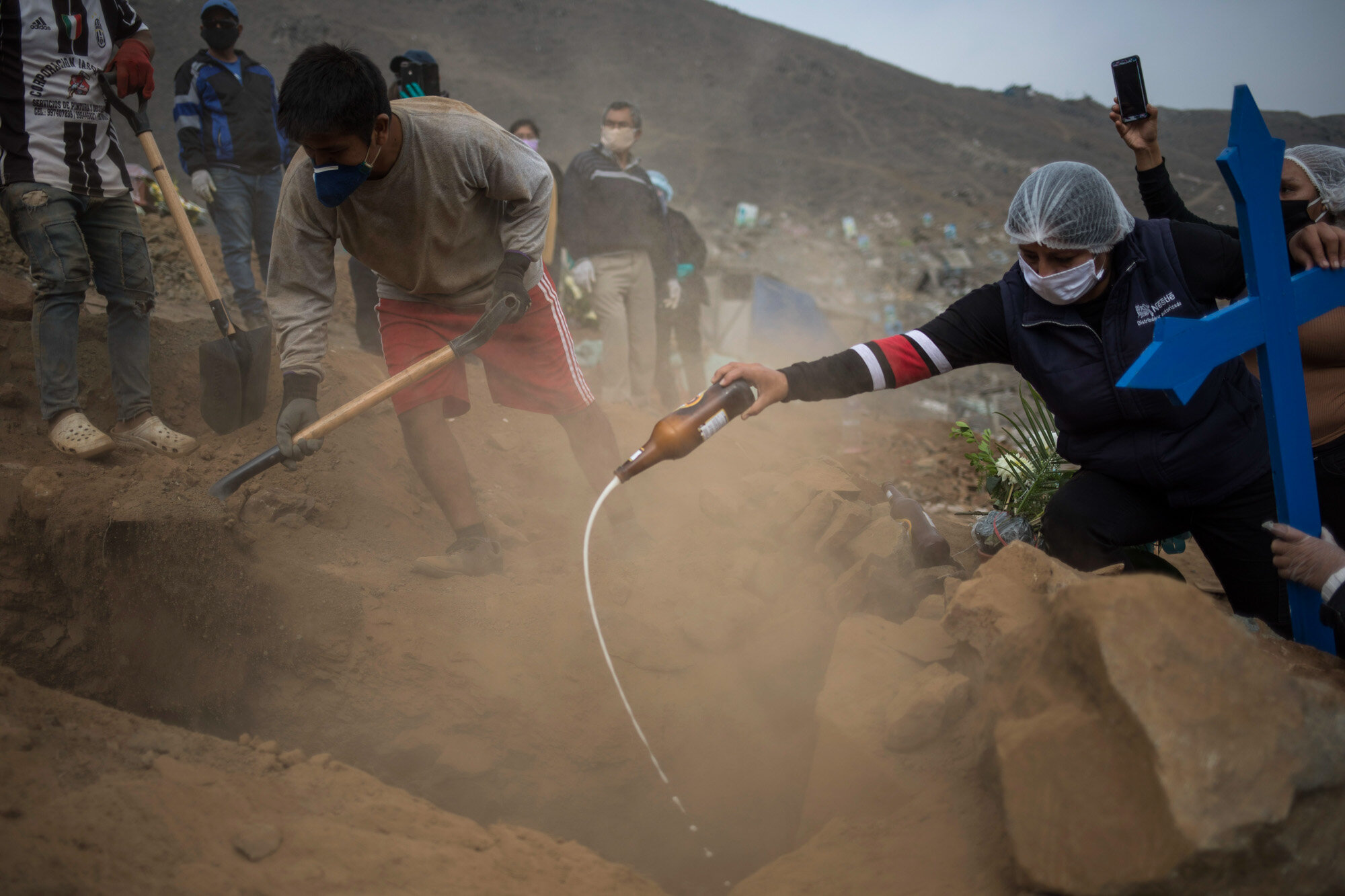 Relatives pour beer into the tomb of Victor Gaspar, who died of COVID-19, during his burial at the Nueva Esperanza cemetery on the outskirts of Lima, Peru, on May 28, 2020. (AP Photo Rodrigo Abd)