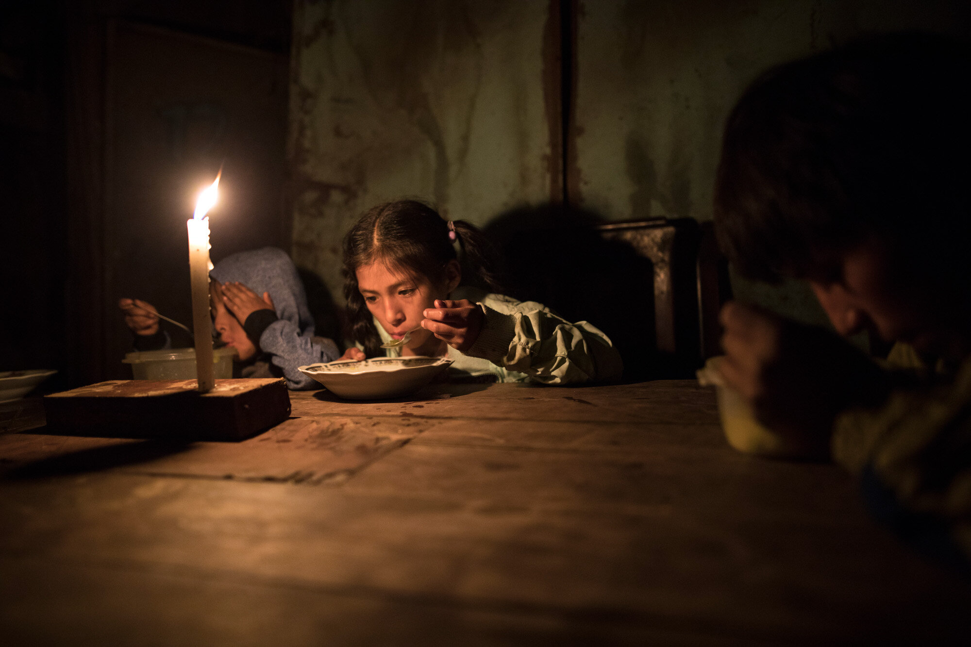  Siblings, from left, Estiben, Estefany and Javier Aquino eat dinner illuminated by a candle in their home in the Nueva Esperanza neighborhood, which has no access to electricity, in Lima, Peru, on June 8, 2020. (AP Photo/Rodrigo Abd) 
