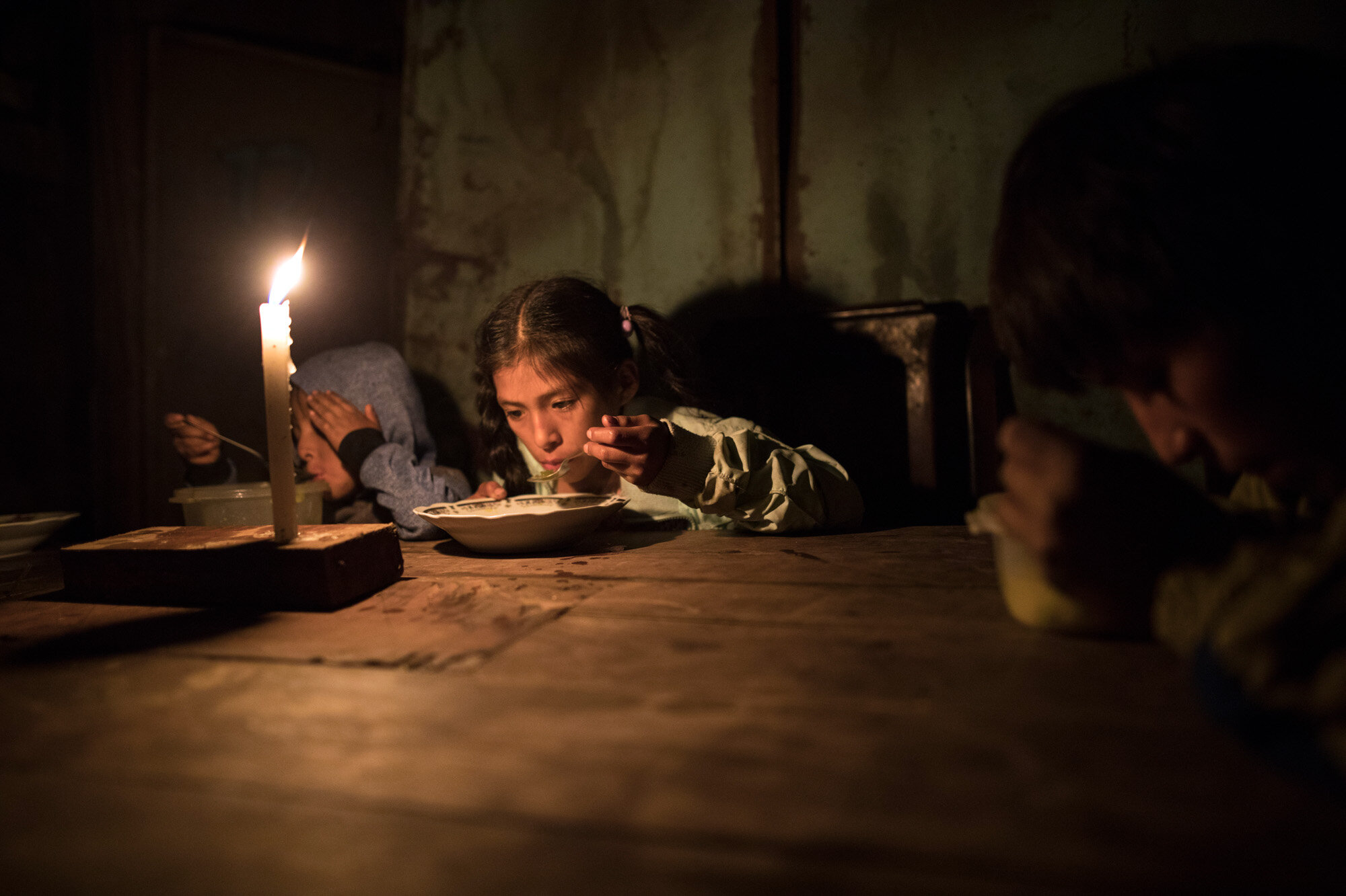 Siblings, from left, Estiben, Estefany and Javier Aquino eat dinner illuminated by a candle in their home in the Nueva Esperanza neighborhood, which has no access to electricity, in Lima, Peru, on June 8, 2020. (AP Photo/Rodrigo Abd)