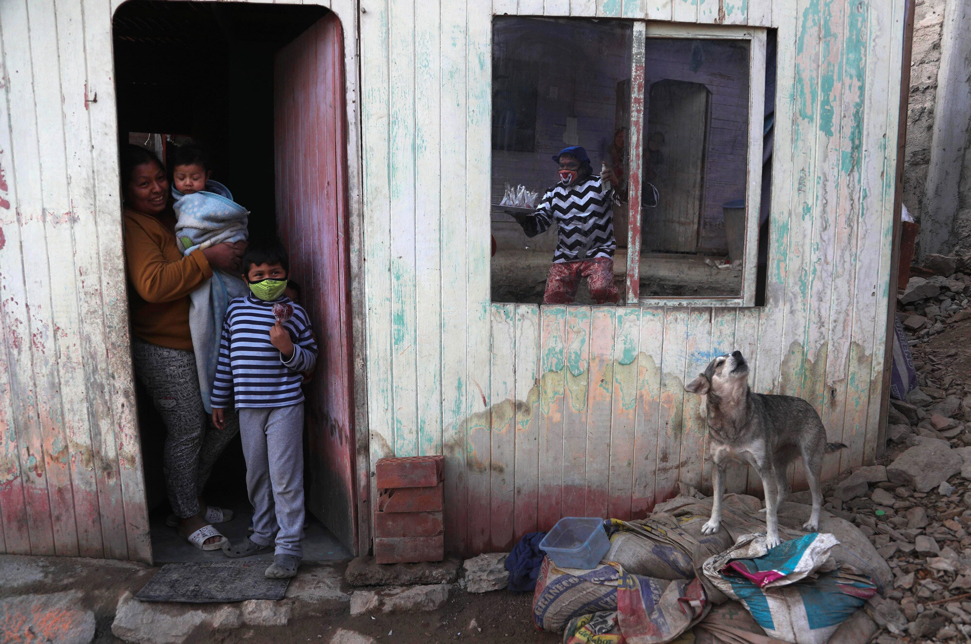 Jhona Zapata, whose clown name is "Jijolin," is reflected in the window of a home as he offers caramelized apples for sale, in a poor neighborhood on the outskirts of Lima, Peru, on Aug. 5, 2020. Zapata, 35, is selling circus food to help his family survive the economic shutdown while circuses are closed to curb the spread of the coronavirus. (AP Photo/Martin Mejia)