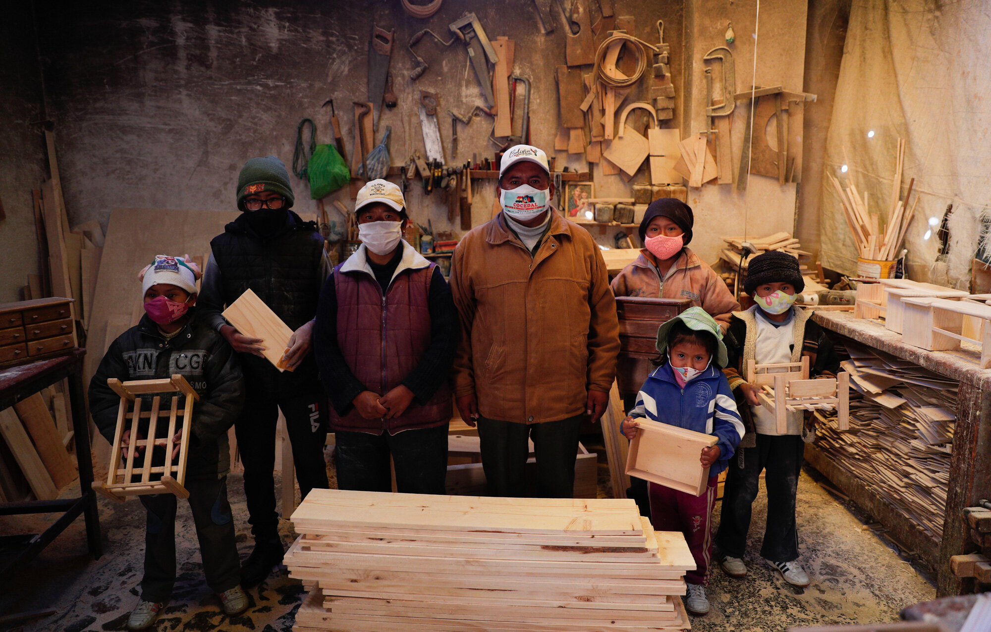 Wearing masks to curb the spread of the coronavirus, the Delgado family poses for a photo in their workshop in El Alto, Bolivia, on Aug. 28, 2020. The five children, from ages 6 and 14, work all day in the family’s small carpentry workshop with their parents. (AP Photo/Juan Karita)