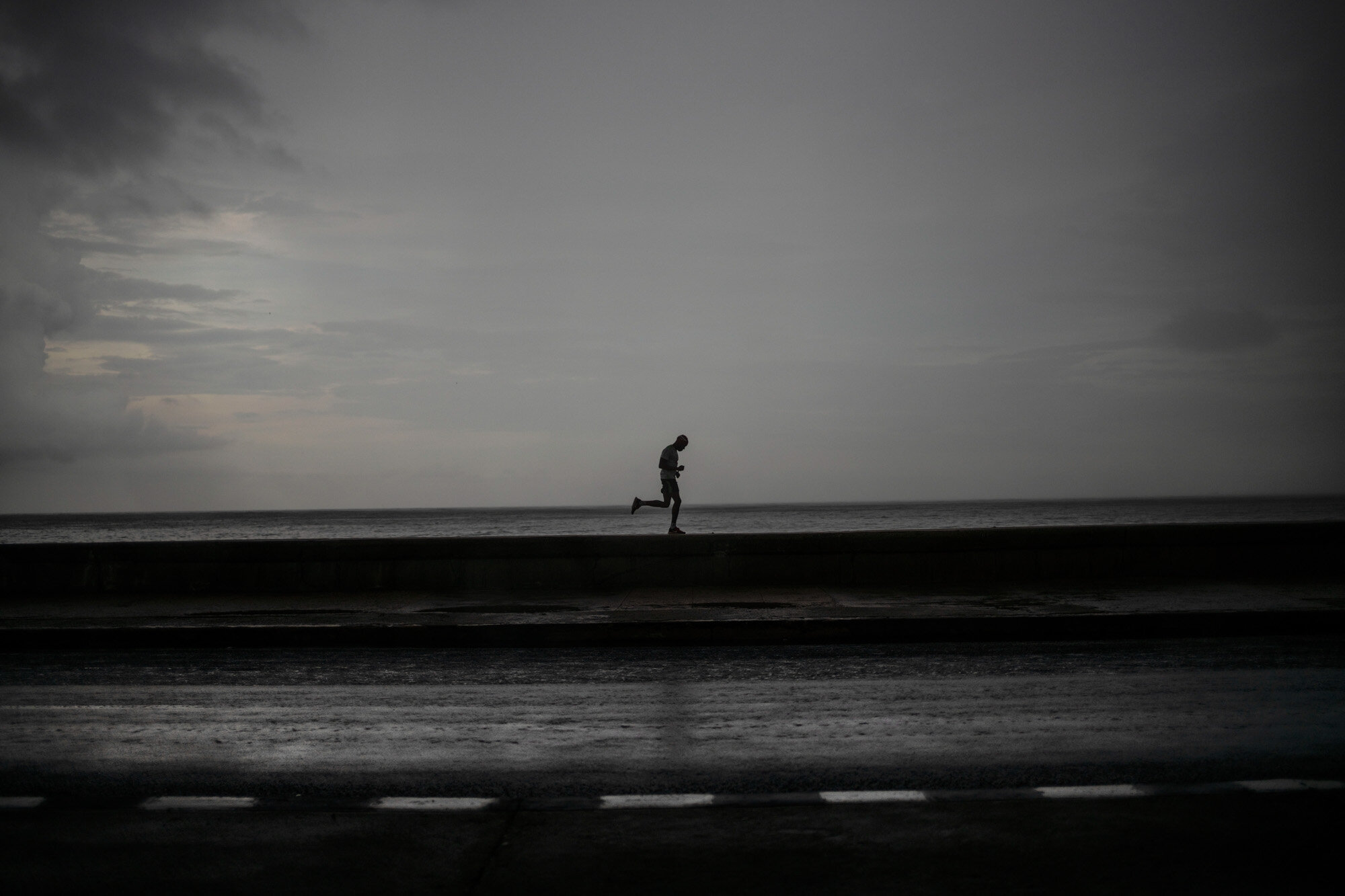 A man wearing a face mask as a precaution against the spread of the coronavirus runs along the Malecon seawall under the rain in Havana, Cuba, on Oct. 6, 2020. (AP Photo/Ramon Espinosa)