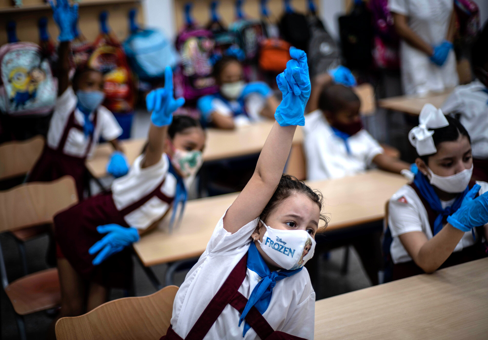 Wearing masks and plastic gloves to prevent the spread of the coronavirus, girls raise their hands during class in Havana, Cuba, on Monday, Nov. 2, 2020. Tens of thousands of school children returned to class Monday in Havana for the first time since April. (AP Photo/Ramon Espinosa)