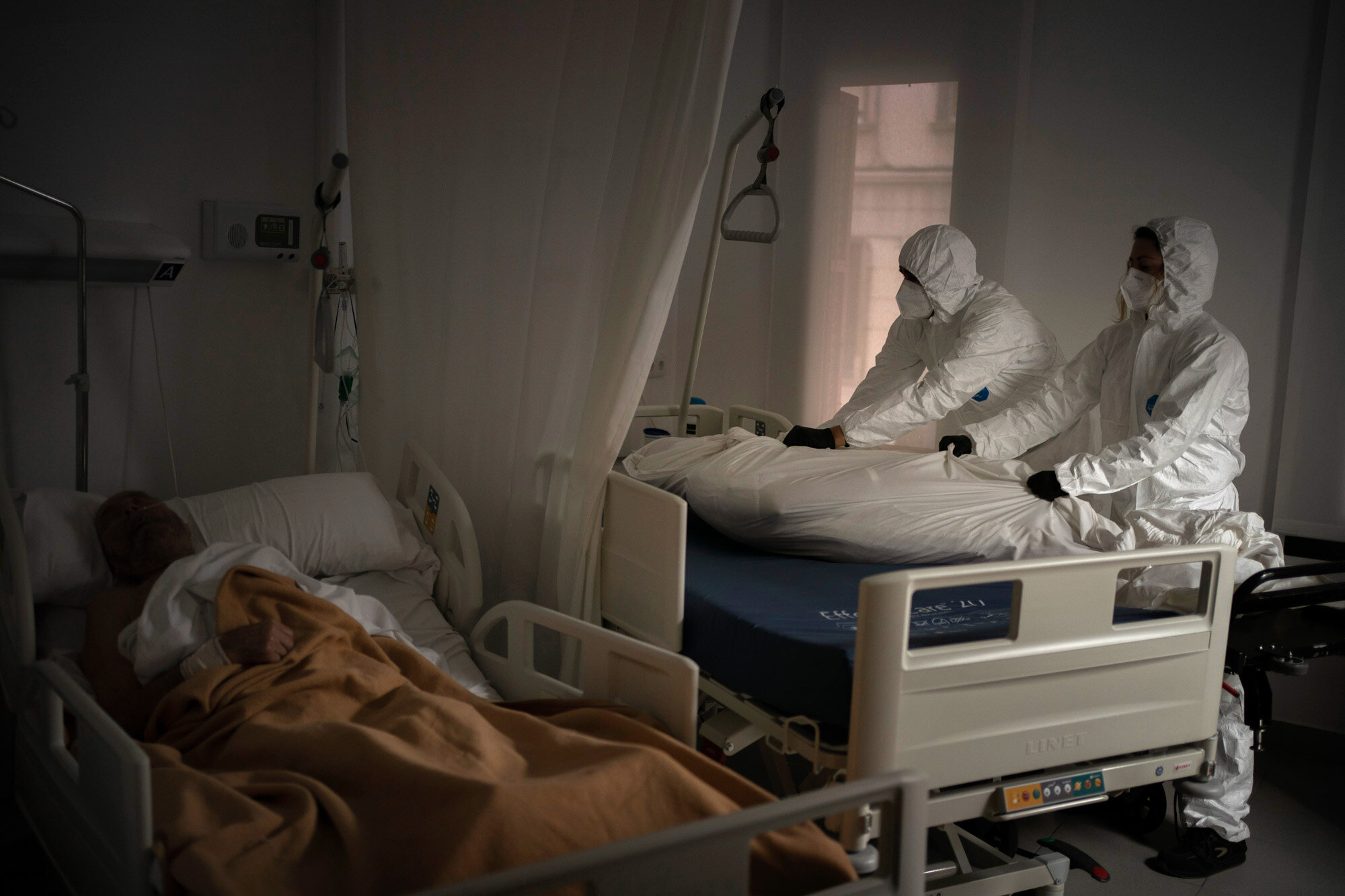 Wearing protective suits to avoid infection, funeral home workers remove the body of an elderly person who died of COVID-19 at a nursing home while another resident sleeps in his bed in Barcelona, Spain, on Nov. 5, 2020. (AP Photo/Emilio Morenatti)