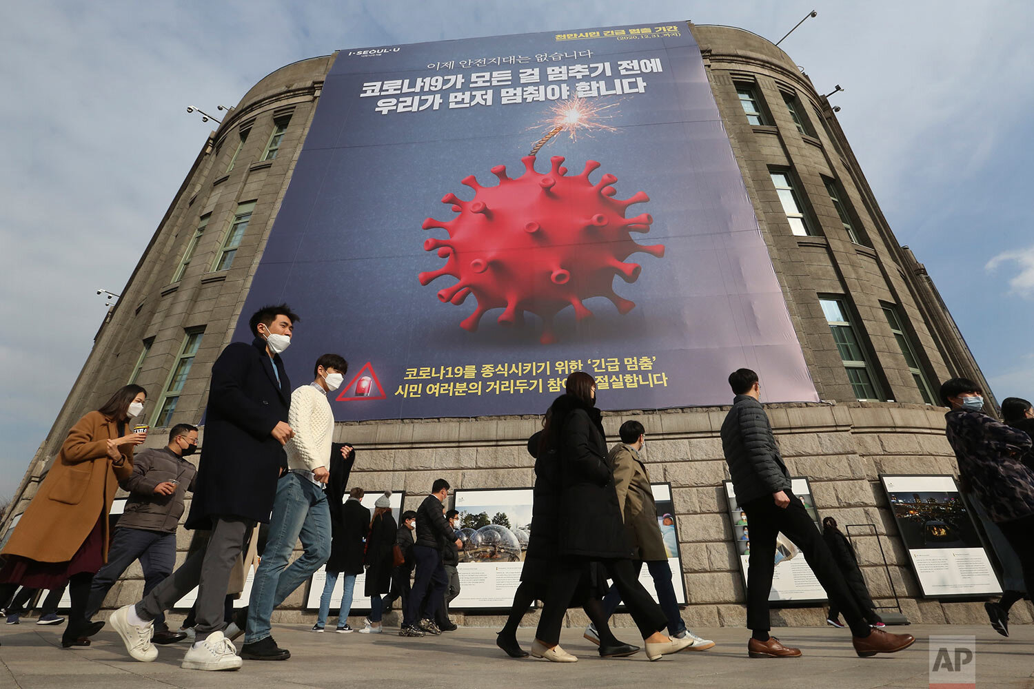  People wearing face masks as a precaution against the coronavirus walk under a banner emphasizing an enhanced social distancing campaign, reading "We have to stop before COVID-19 stops everything, “ in front of Seoul City Hall in Seoul, South Korea,