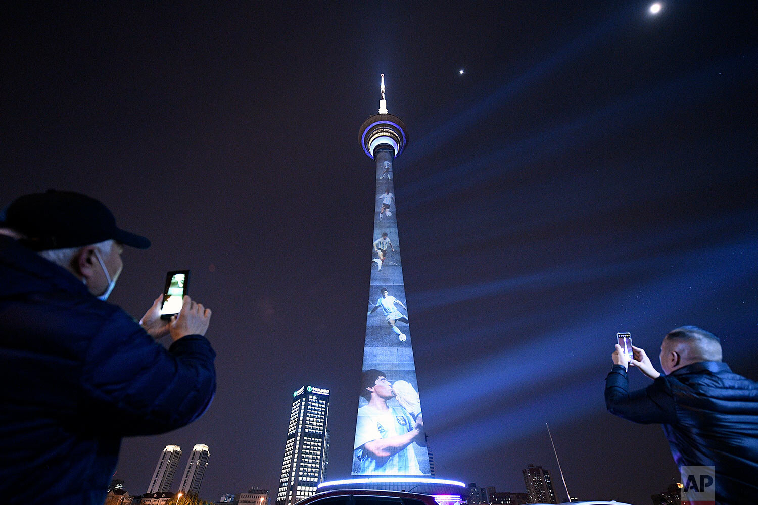  People take photos of images of soccer legend Diego Maradona projected onto a TV tower in Tianjin, China, Thursday, Nov. 26, 2020.  (Chinatopix via AP) 