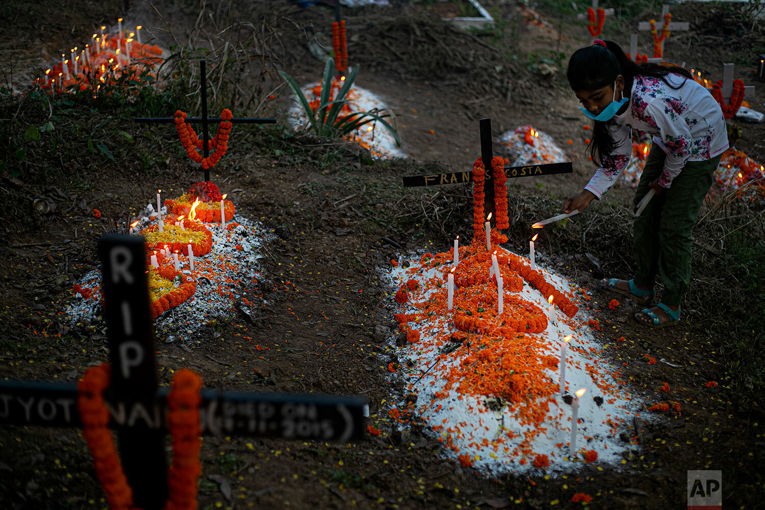  A girl wearing a face mask as a precaution against the coronavirus lights a candle as she prays at the grave of a deceased relative during All Souls Day in Gauhati, India, Monday, Nov. 2, 2020. (AP Photo/Anupam Nath) 
