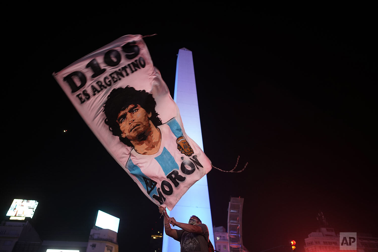  A man waves a banner with the image of Diego Maradona who died from a heart attack at his home at the age of 60, in downtown Buenos Aires, Argentina, Wednesday, Nov. 25, 2020. (AP Photo/Victor Caivano) 