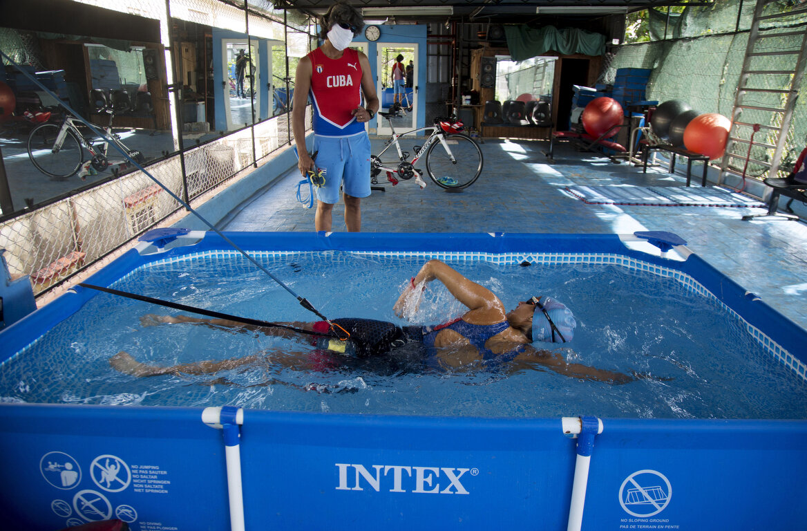  Leslie Amat, a Cuban triathlon athlete, swims in a pool with straps that keep her from advancing, under the watch of her trainer Dioseles Fernandez in the patio of her home in Havana, Cuba, Monday, April 20, 2020. Amat aims to classify for the 2021 