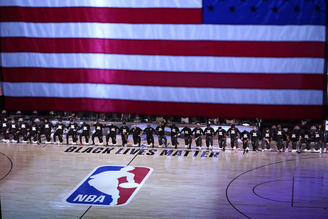  Members of the Orlando Magic and Brooklyn Nets kneel around a Black Lives Matter logo during the national anthem before the start of an NBA basketball game Friday, July 31, 2020, in Lake Buena Vista, Fla. (AP Photo/Ashley Landis, Pool) 