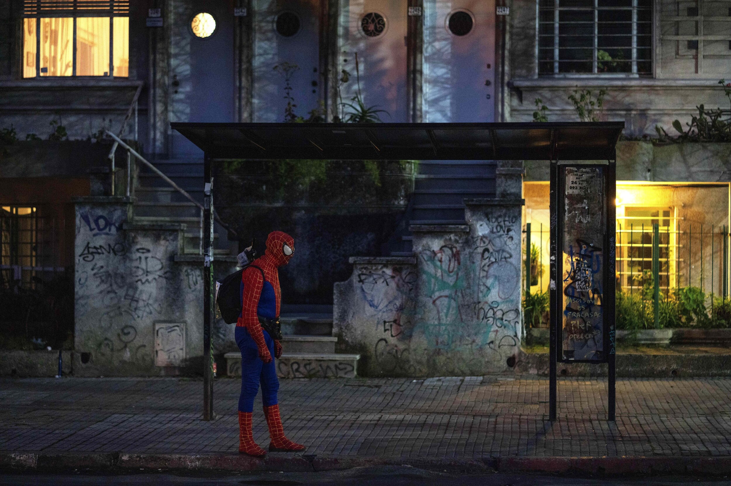  A man in a Spiderman costume waits for the bus in Montevideo, Uruguay, Sunday, Aug. 2, 2020, the night before the reopening of cinemas, theaters and museums that were closed to curb the spread of the new coronavirus. (AP Photo/Matilde Campodonico) 