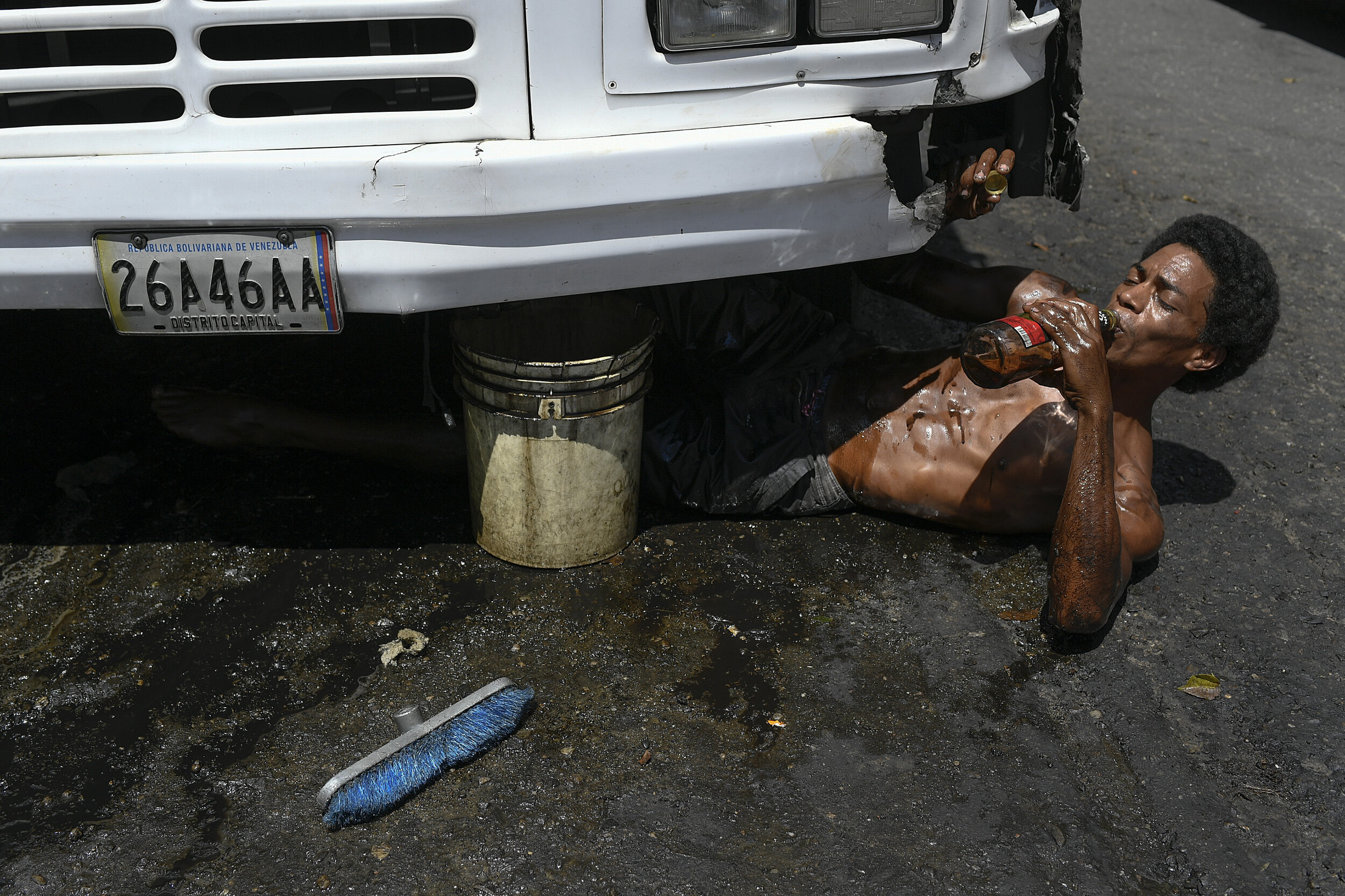  Jose Gregorio Machado takes a sip of rum while cleaning the underside of a bus in the Petare neighborhood of Caracas, Venezuela, Saturday, Oct. 17, 2020. Machado cleans buses for $5 U.S. dollars per bus. He says that on a good day he gets to clean s
