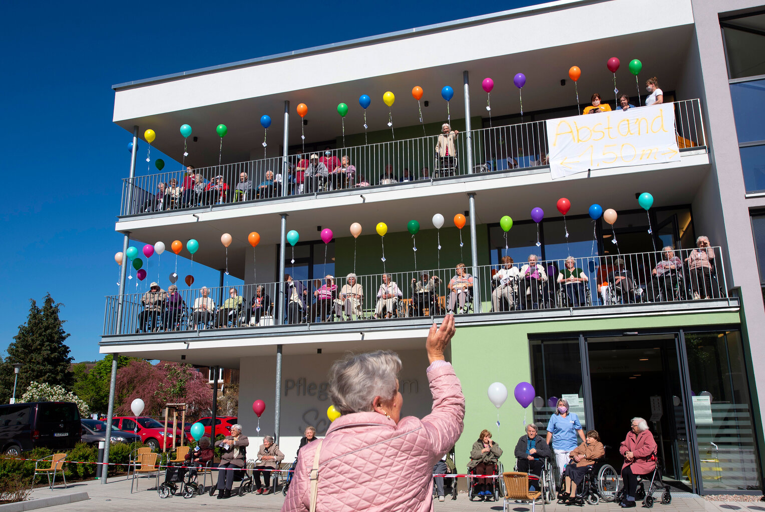  A woman waves to nursing home residents and nurses as they attend a service of the protestant church under the theme 'Glimmer of hope' in front of the nursing centre Schanzehof in Tiefenort, central Germany, Thursday, May 7, 2020. (AP Photo/Jens Mey