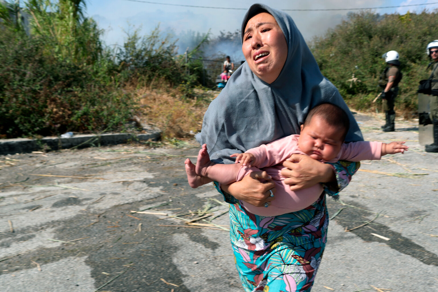  A migrant holds her baby as she runs to avoid a small fire in a field near Mytilene town, on the northeastern island of Lesbos, Greece, Saturday, Sept. 12, 2020. (AP Photo/Petros Giannakouris) 