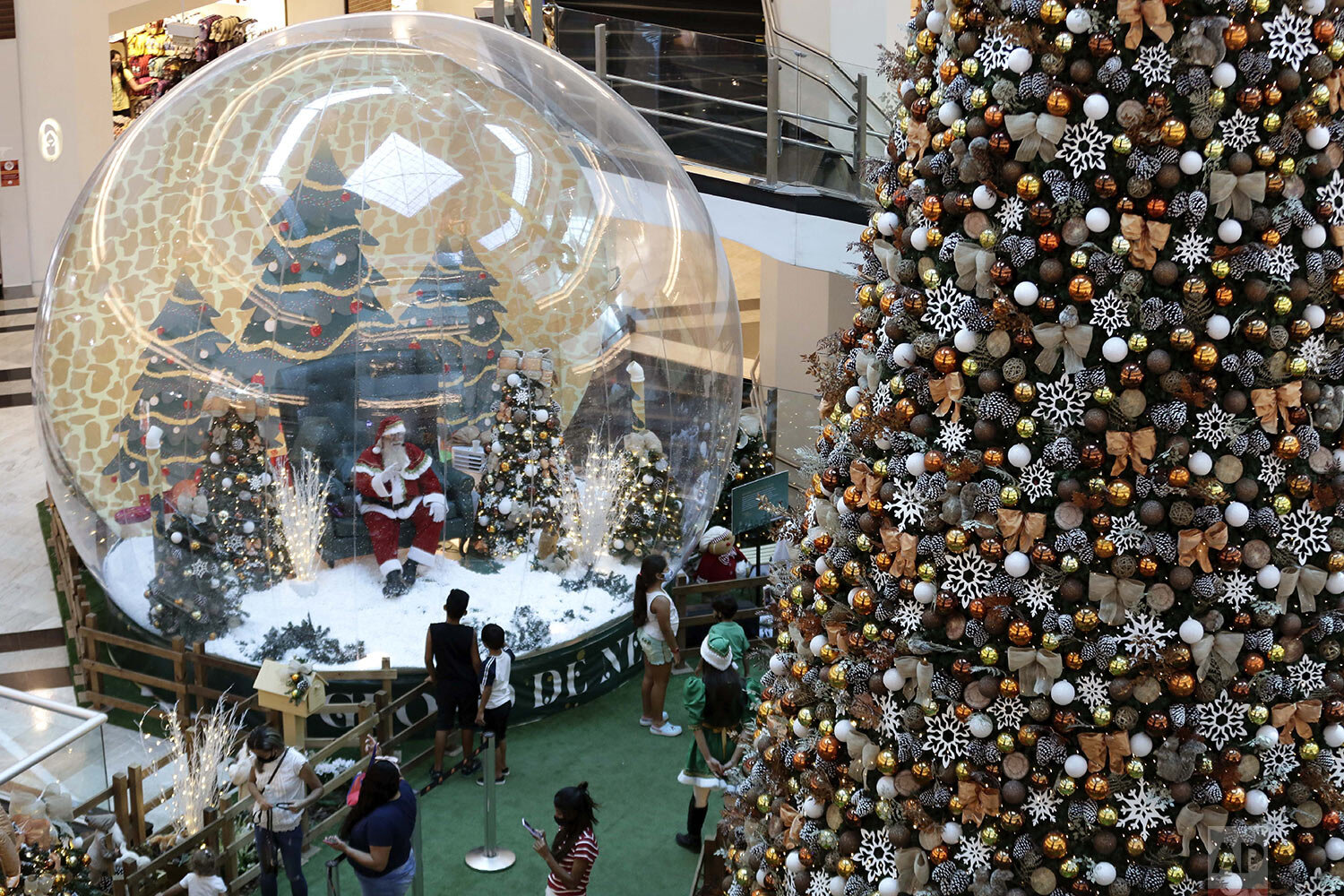 Santa Claus performer Abilio Nunes greets a child from inside a life-size snow globe, as a protective measure amid the spread of COVID-19, at a shopping center in Brasilia, Brazil, Wednesday, Dec. 16, 2020. (AP Photo/Eraldo Peres)