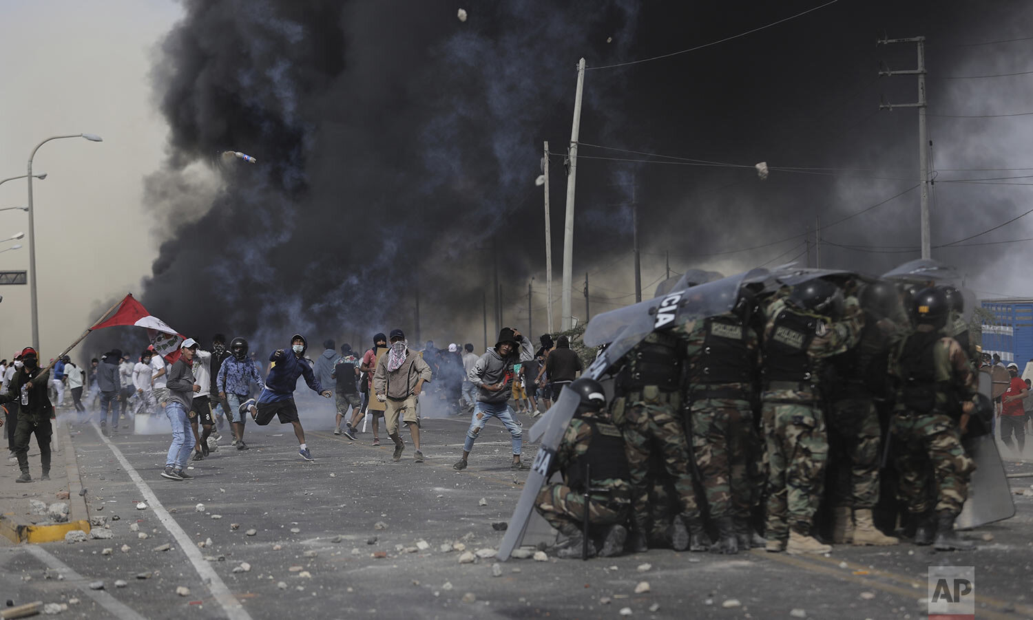 Farmworkers throw rocks at police trying to remove them from the Pan-American South Highway as they protest the Agricultural Promotion Law in the Barrio Chino neighborhood of Peru's Ica province, Tuesday, Dec. 22, 2020. Farmworkers are demanding better pay and protesting clauses in a law that exempts them from benefits given to other workers, including annual bonuses and paid vacation. (AP Photo/Luis Campos)