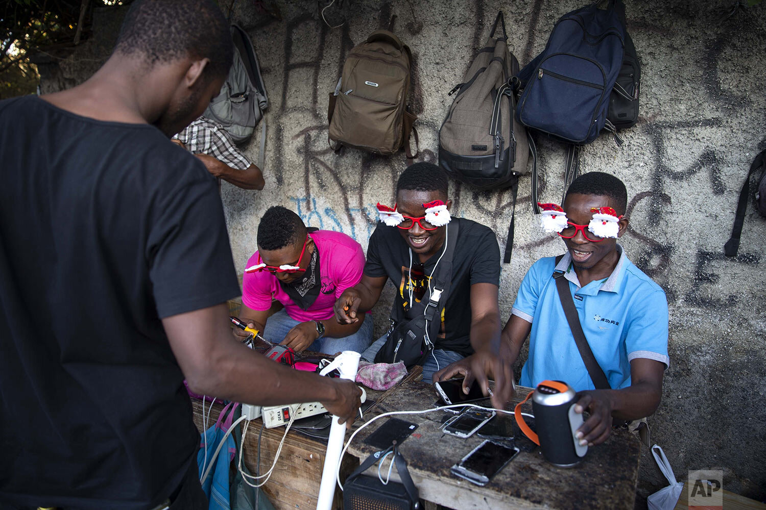 Cellphone repairmen wear Santa Clause themed glasses as they ply their trade on the sidewalk in Port-au-Prince, Haiti, Thursday, Dec. 24, 2020. (AP Photo/ Dieu Nalio Chery)