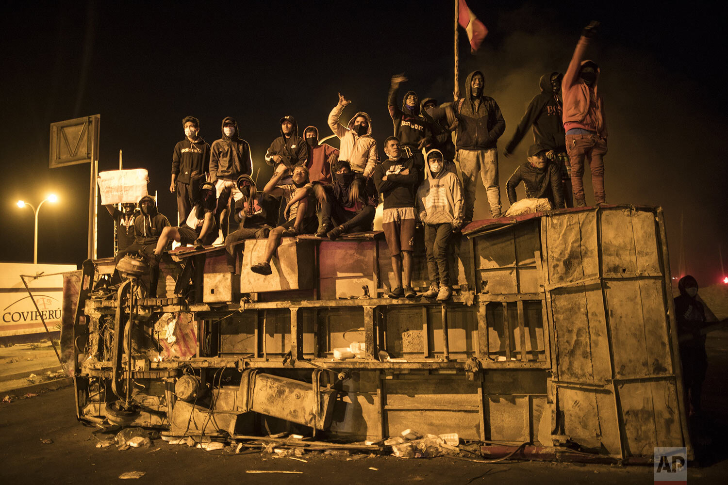 Farmworkers stand atop an overturned bus blocking the Pan-American highway as they protest for better salaries and health benefits in Villacuri, Ica province, Peru, early Friday, Dec. 4, 2020. (AP Photo/Rodrigo Abd)