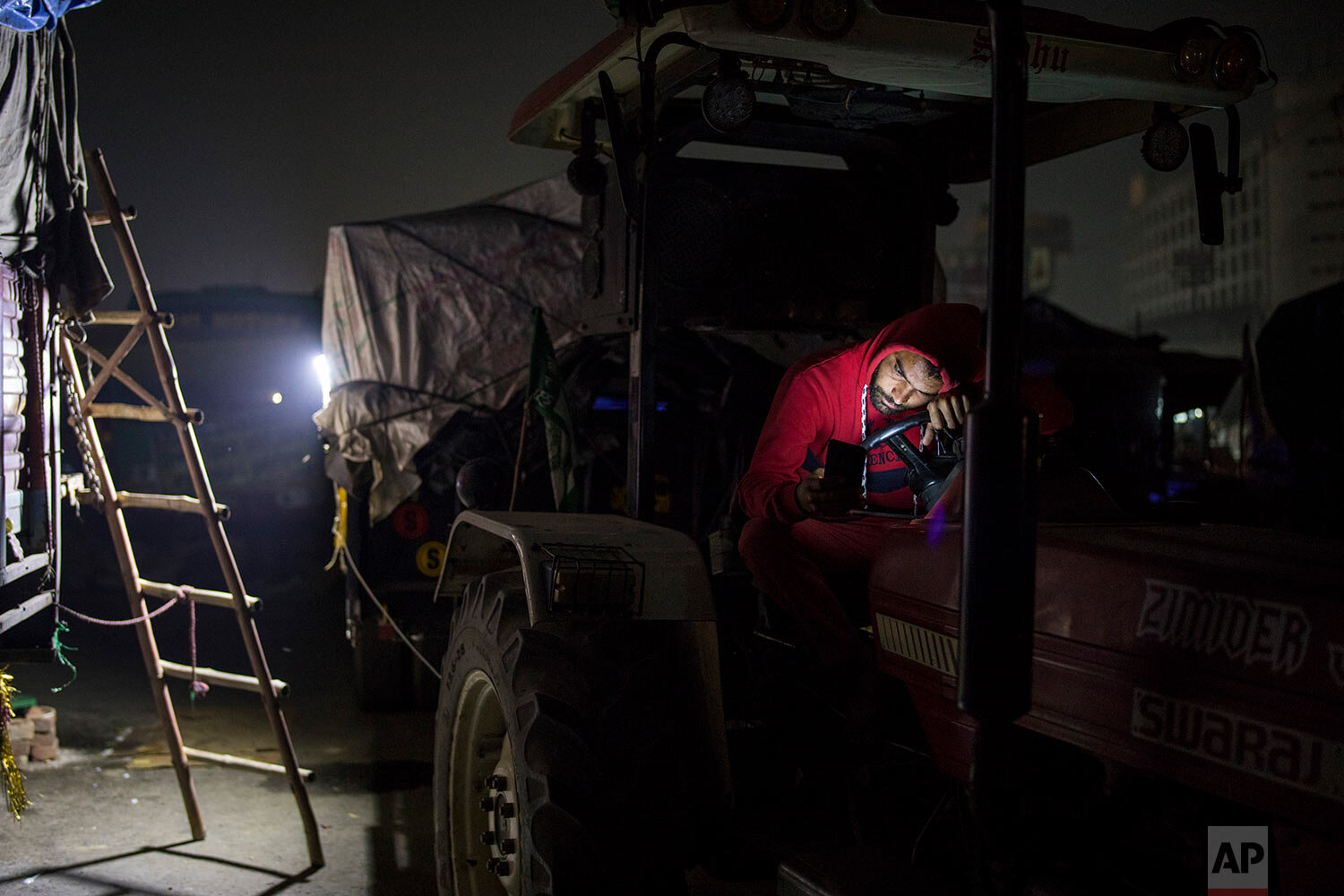  Farmer Brijender Singh, 24, looks at his mobile phone while sitting on his tractor parked on a highway during a protest at the Delhi-Haryana state border, India, Wednesday, Dec. 2, 2020.  (AP Photo/Altaf Qadri) 