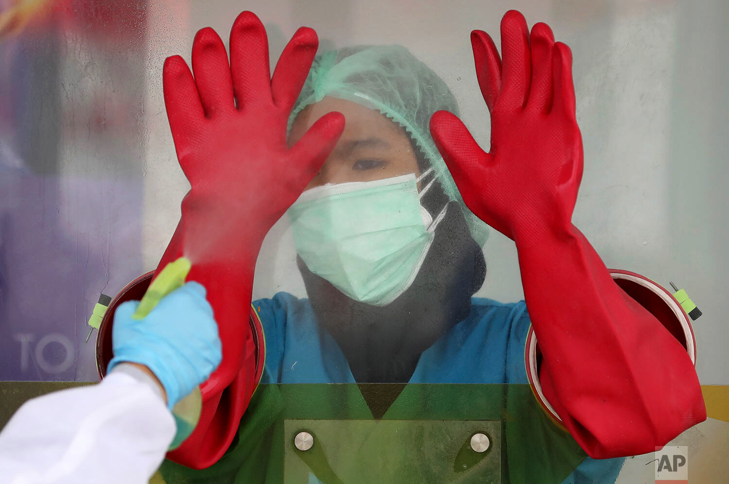  A medical worker is assisted by a colleague to have her rubber gloves sprayed with disinfectant at a walk-through coronavirus test site at Genomik Solidaritas Indonesia Laboratory in Jakarta, Indonesia, Monday, Dec. 14, 2020.  (AP Photo/Dita Alangka