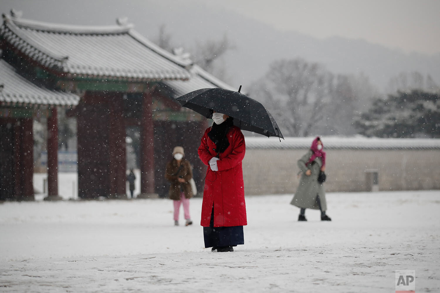  An employee wearing a face mask as a precaution against the coronavirus uses an umbrella to take shelter from the snow at the Gyeongbok Palace, one of South Korea's well-known landmarks, in Seoul, South Korea, Sunday, Dec. 13, 2020. (AP Photo/Lee Ji