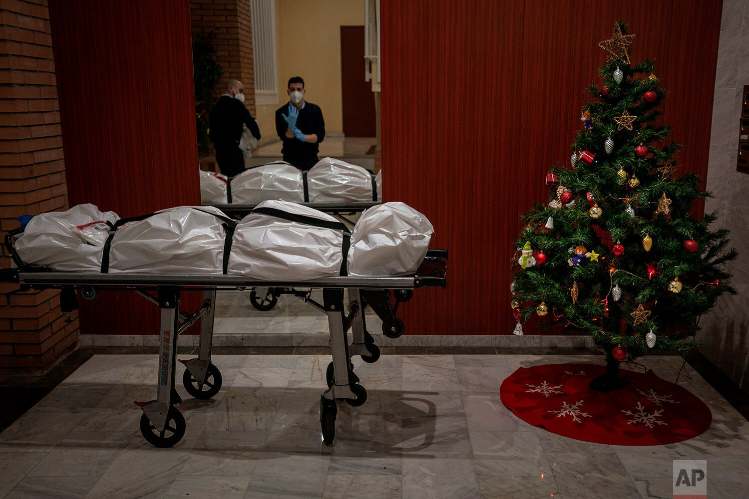  Mortuary workers take off their protective clothing at the entrance of a building decorated with a Christmas tree, after removing the body of person who is suspected of dying from COVID-19 in Barcelona, Spain, Wednesday, Dec. 23, 2020. (AP Photo/Emi