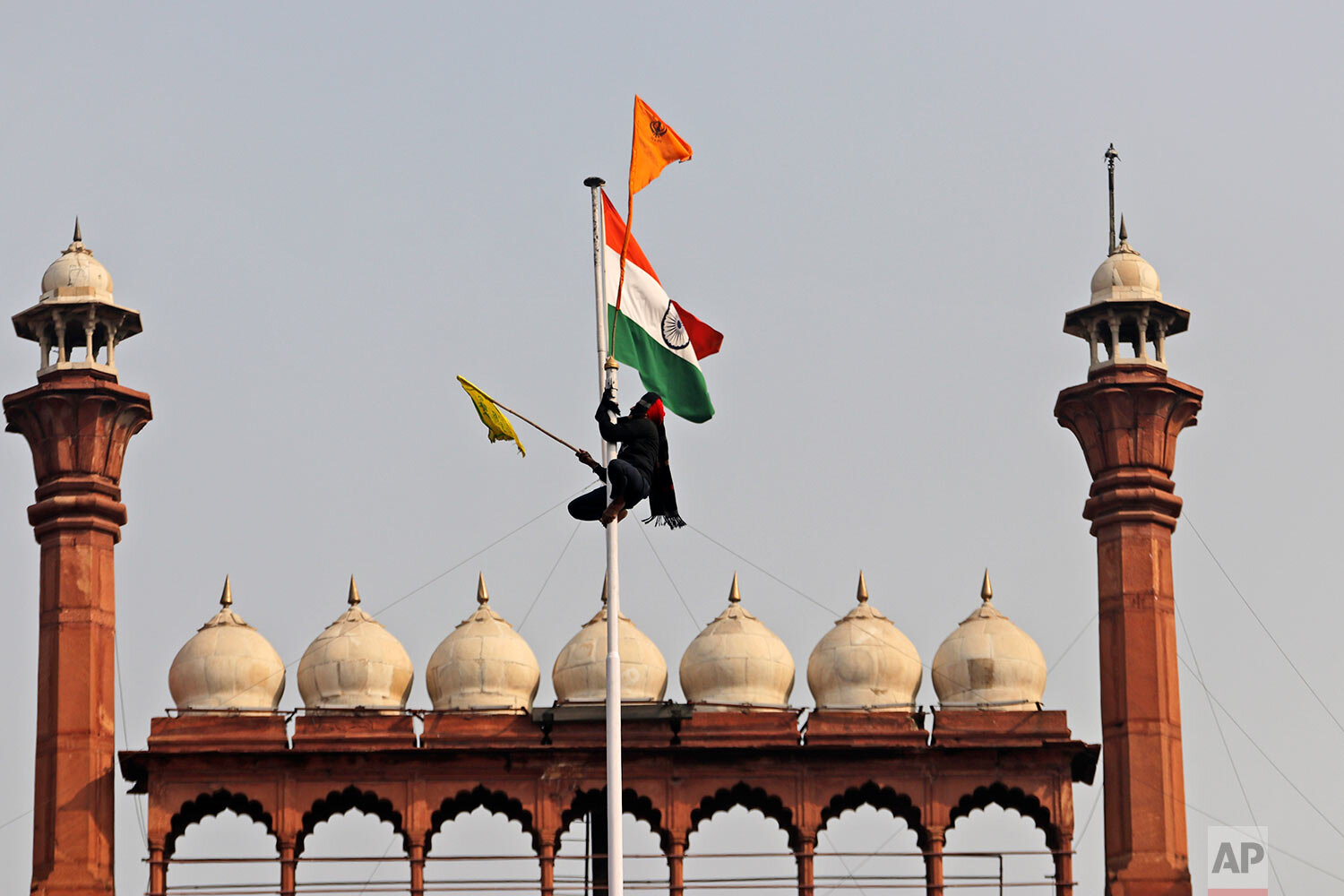  A Sikh man hangs on to a pole holding a Sikh religious flag along with a farm union flag at the historic Red Fort monument in New Delhi, India, Tuesday, Jan. 26, 2021. (AP Photo/Supreet Sapkal) 