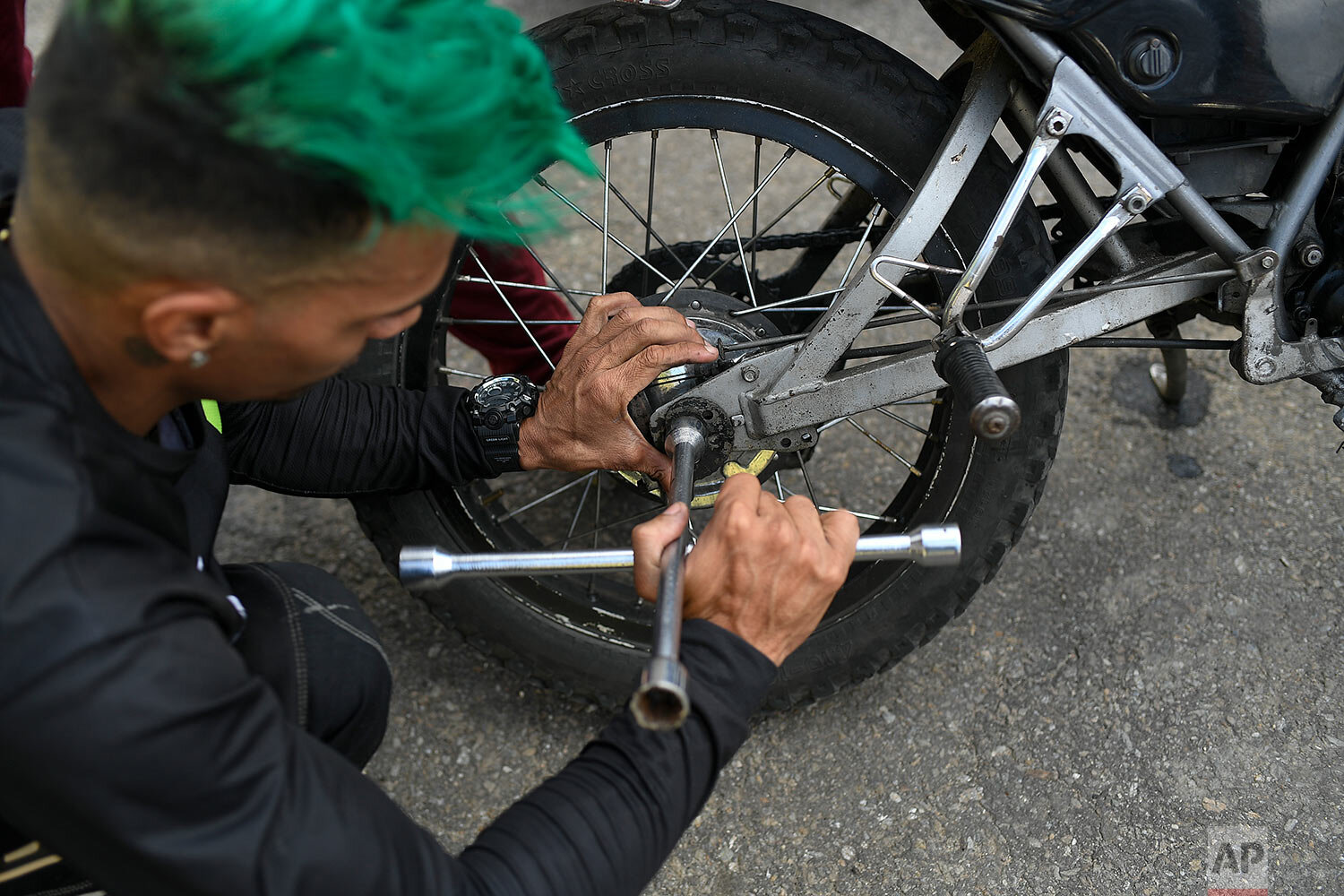  Motorcycle stuntman Pedro Aldana fixes his brakes during an exhibition in the Ojo de Agua neighborhood of Caracas, Venezuela, Sunday, Jan. 10, 2021. (AP Photo/Matias Delacroix) 
