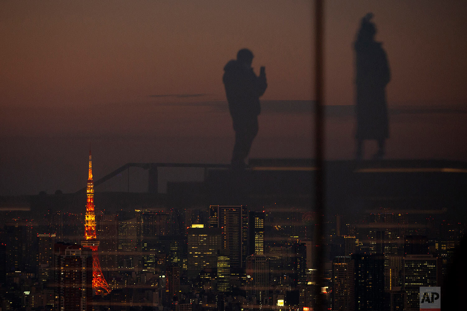  Silhouetted against the warm sunset skyline and the illuminated Tokyo Tower, visitors are reflected on the glass walls of a rooftop observation deck Thursday, Jan. 21, 2021, in Tokyo. (AP Photo/Kiichiro Sato) 