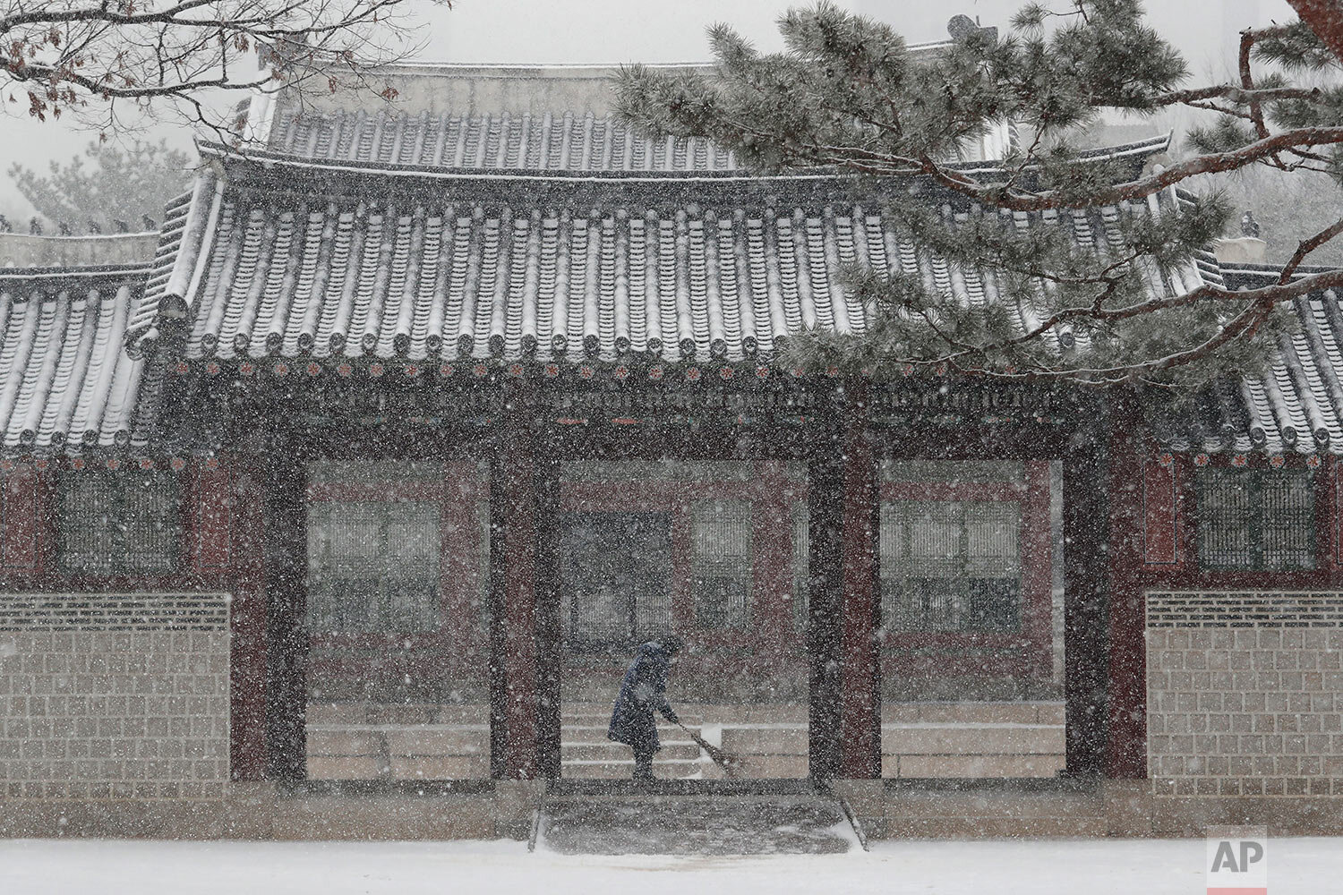 A worker wearing a face mask as a precaution against the coronavirus sweeps snow off the walkways with a broom at the Deoksu Palace in Seoul, South Korea, Tuesday, Jan. 12, 2021. (AP Photo/Ahn Young-joon) 