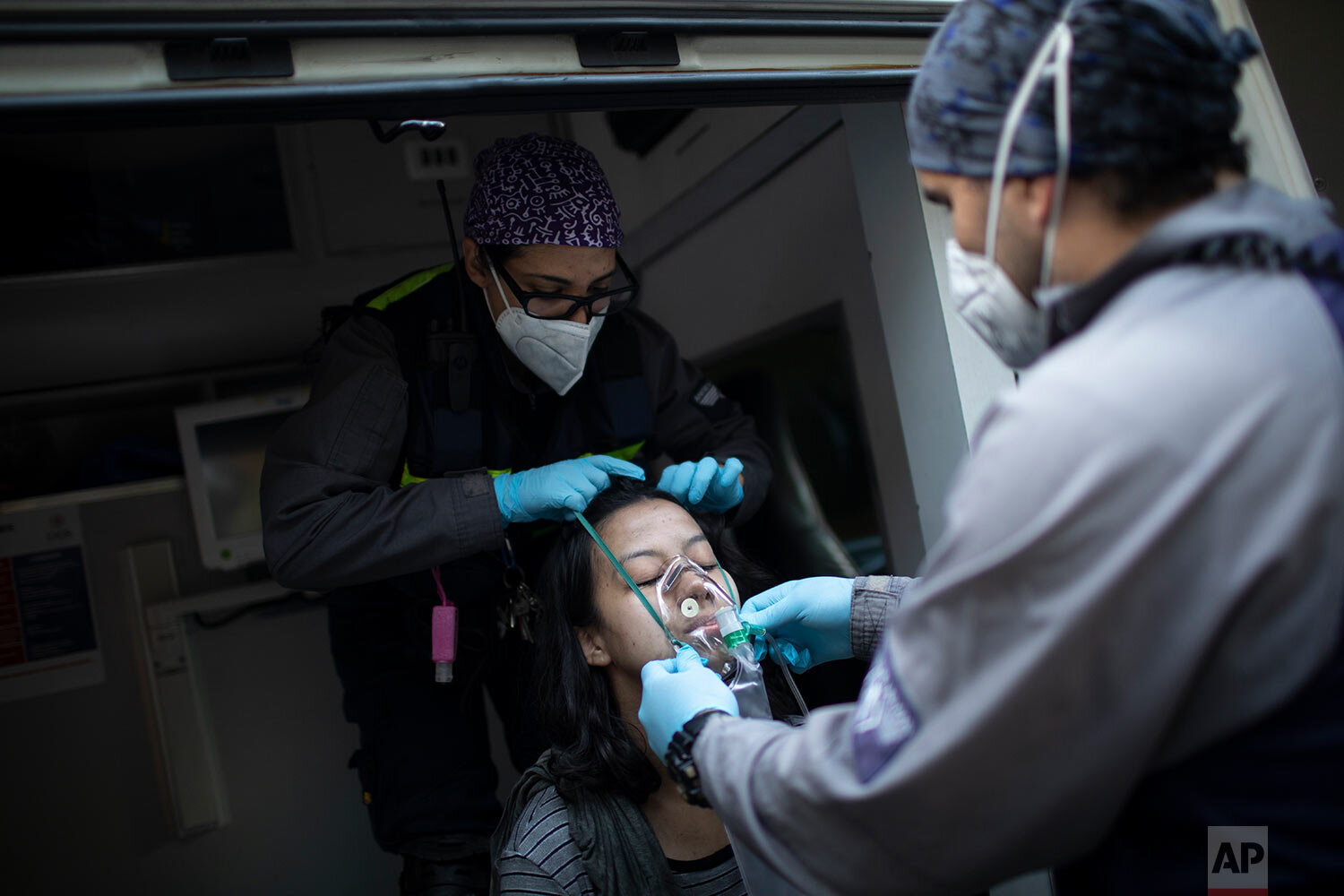  Wearing masks as a precaution against the new coronavirus, Angels of the Road volunteer paramedics Rodolfo Alvarado, right, and Zully Rodiz, place an oxygen mask on a woman who was in a residential building when a car burst into flames in the parkin