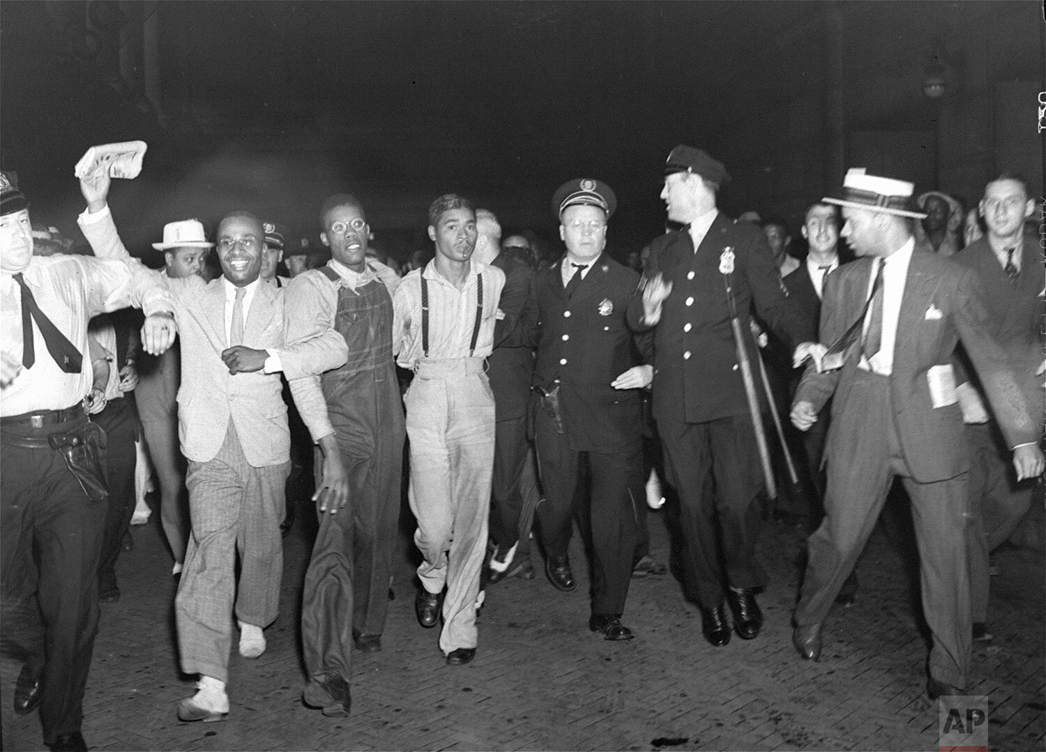  In this July 26, 1937 photo, police escort two of the five recently freed "Scottsboro Boys," Olen Montgomery, wearing glasses, third left, and Eugene Williams, wearing suspenders, forth left through the crowd greeting them upon their arrival at Penn